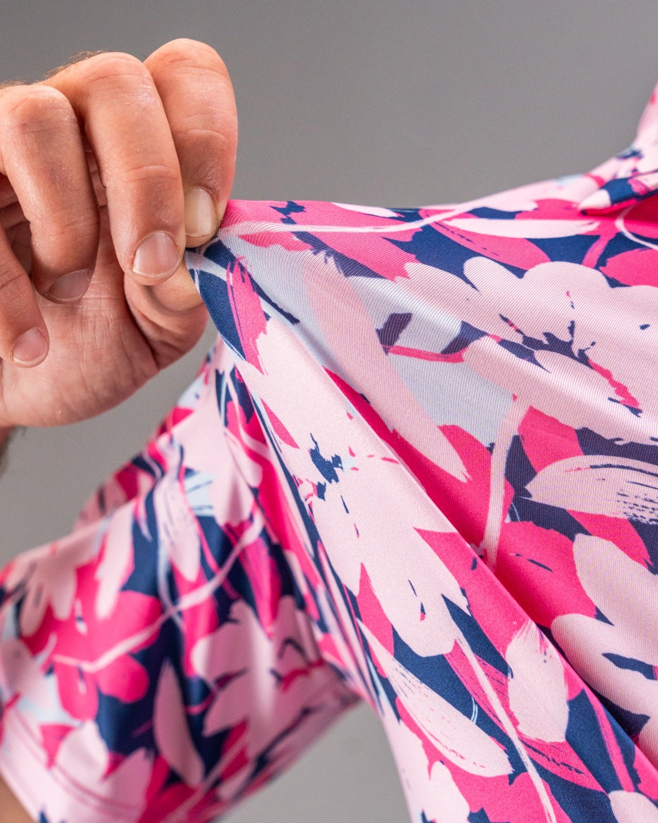 Close-up of a hand pulling the fabric of a pink floral golf shirt, showcasing its vibrant brushed flower design.