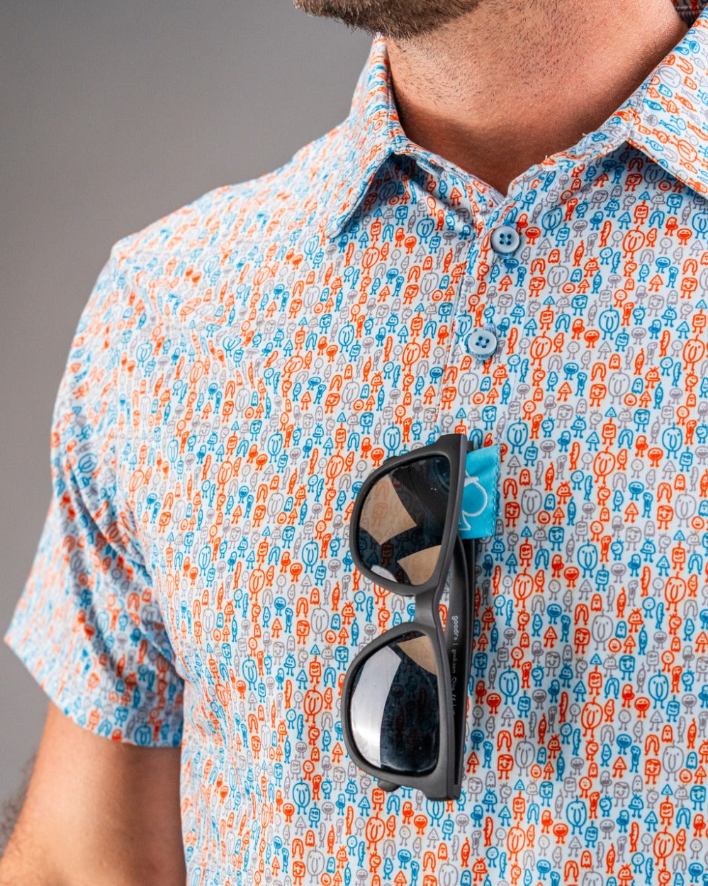 Close-up of a colorful, patterned golf shirt with blue, orange, and gray figures, and black sunglasses clipped to the chest.