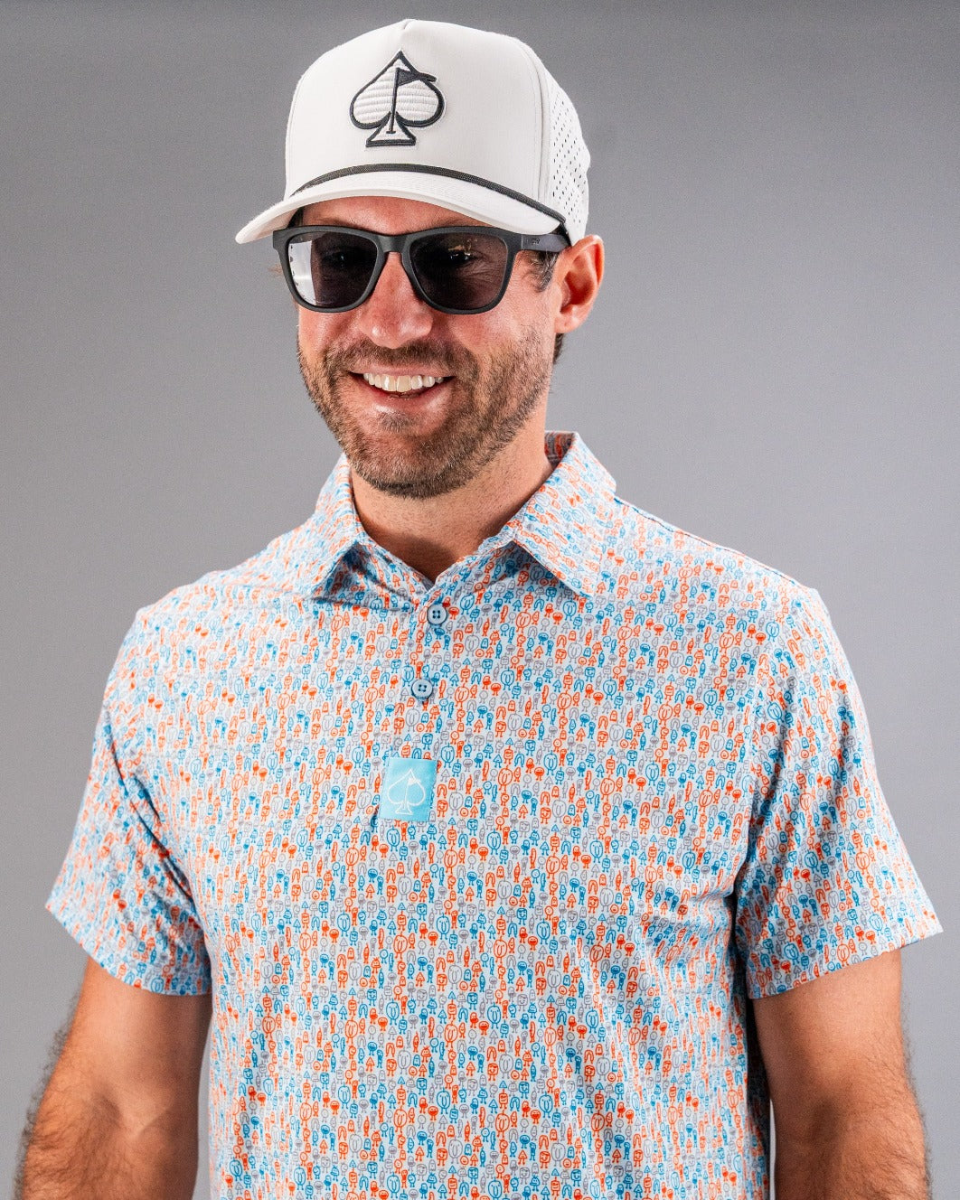 Bold blue golf shirt featuring a playful doodle pattern, paired with a stylish cap and sunglasses for a standout look.
