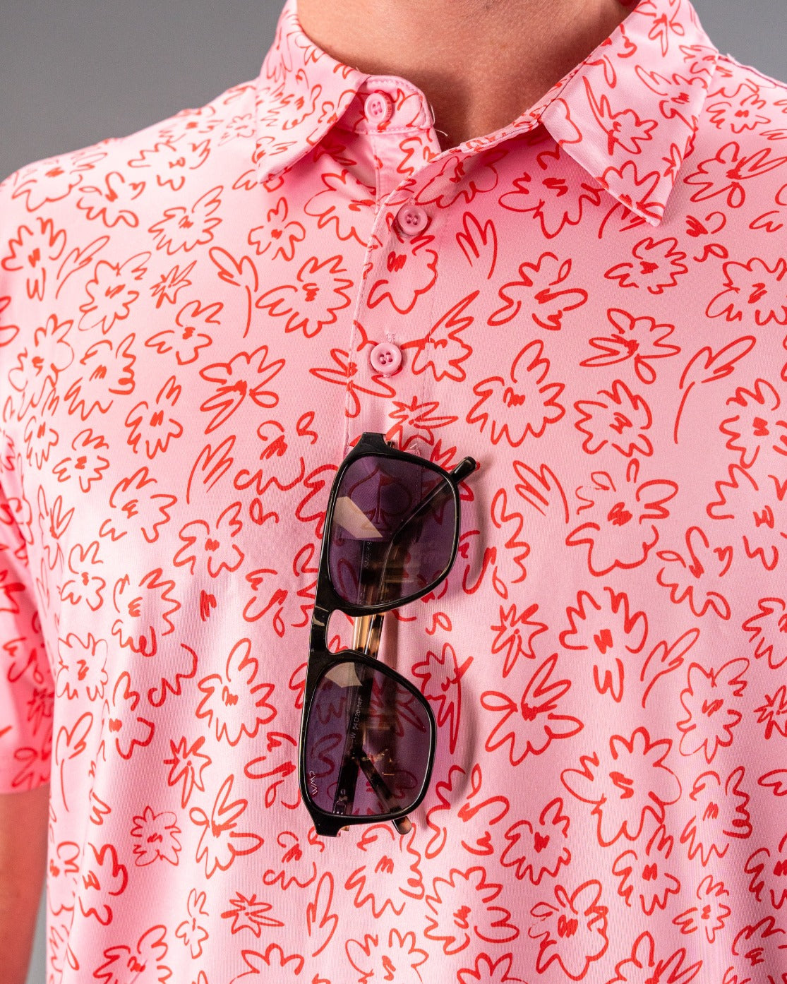 Men's pink golf shirt featuring a vibrant flower doodle pattern, paired with stylish sunglasses for a bold look.