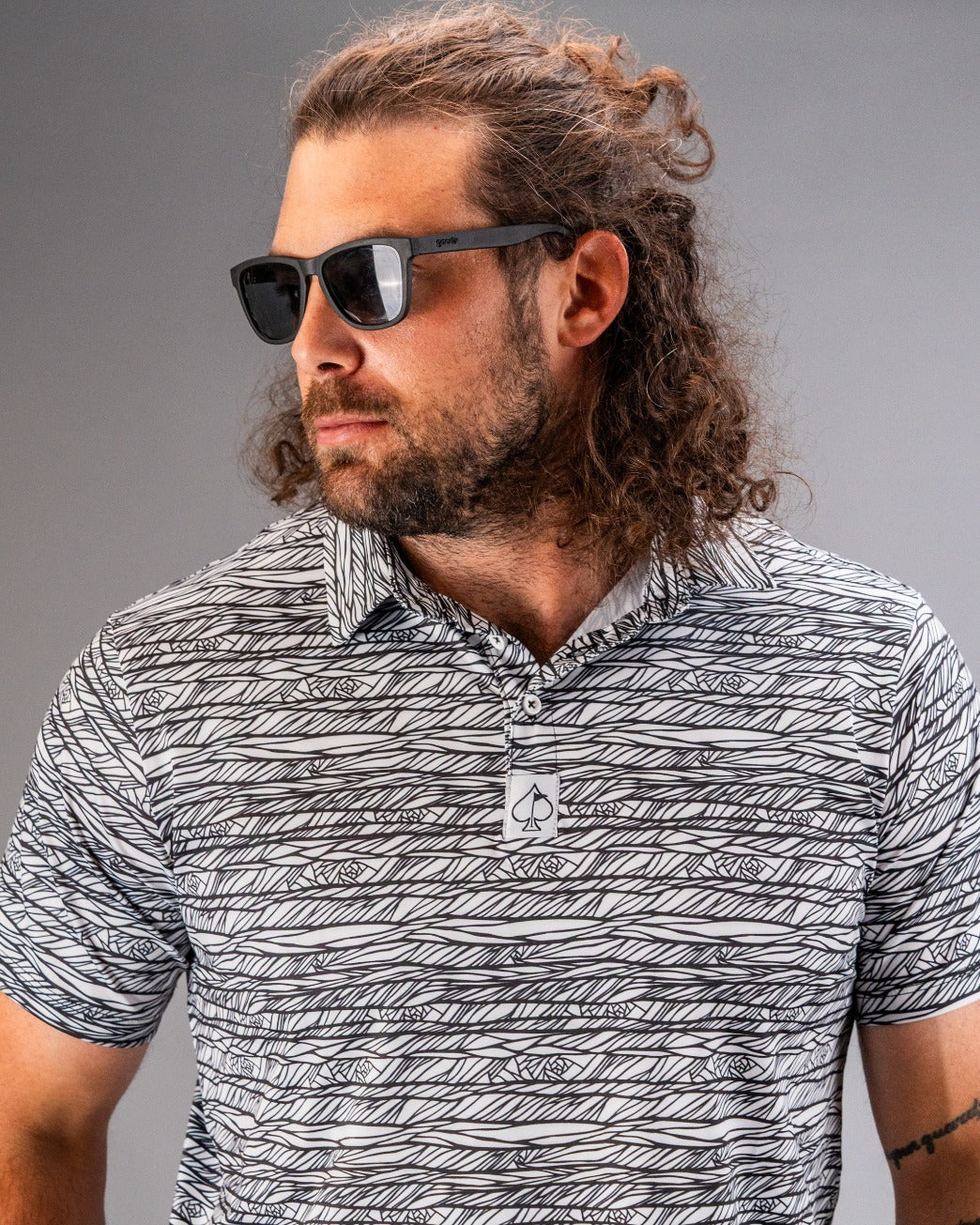 Stylish man wearing a black and white patterned golf polo with sunglasses, showcasing bold golf fashion.