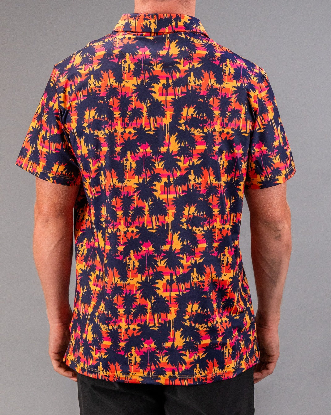 Vibrant tropical print golf shirt with black palm trees, pink, orange, and yellow sunset hues, perfect for bold golf style.