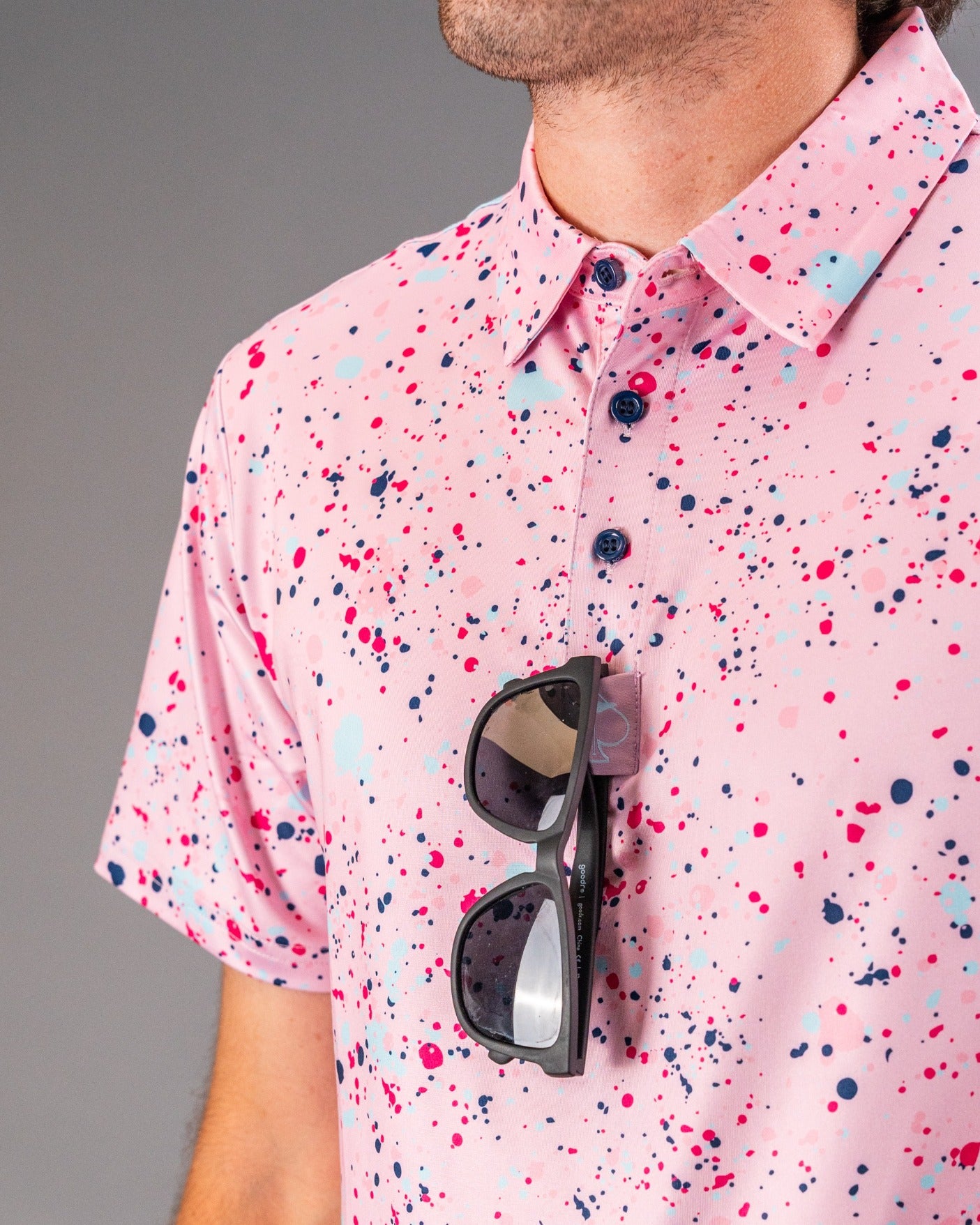 Men's pink splatter golf shirt featuring a vibrant design with blue and navy accents, paired with stylish sunglasses.