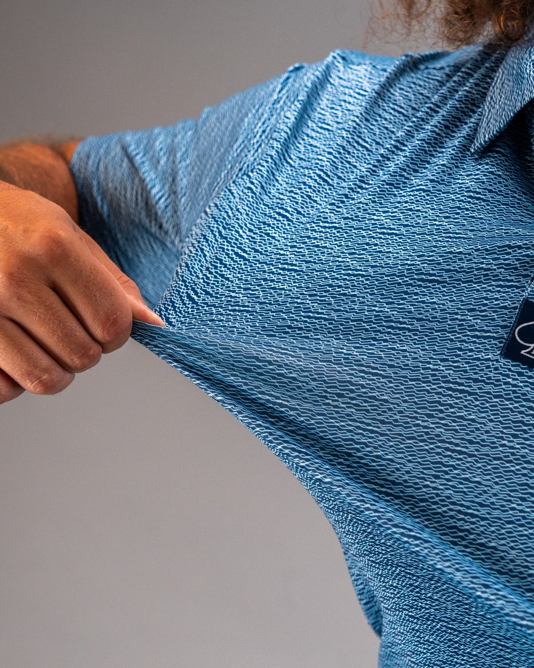 Close-up of a person stretching a light blue golf shirt with a textured squiggle pattern, showcasing its flexibility and style.