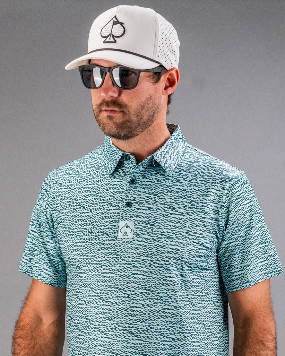 Teal golf polo with a squiggle pattern, paired with a white cap and sunglasses, perfect for stylish golfers.