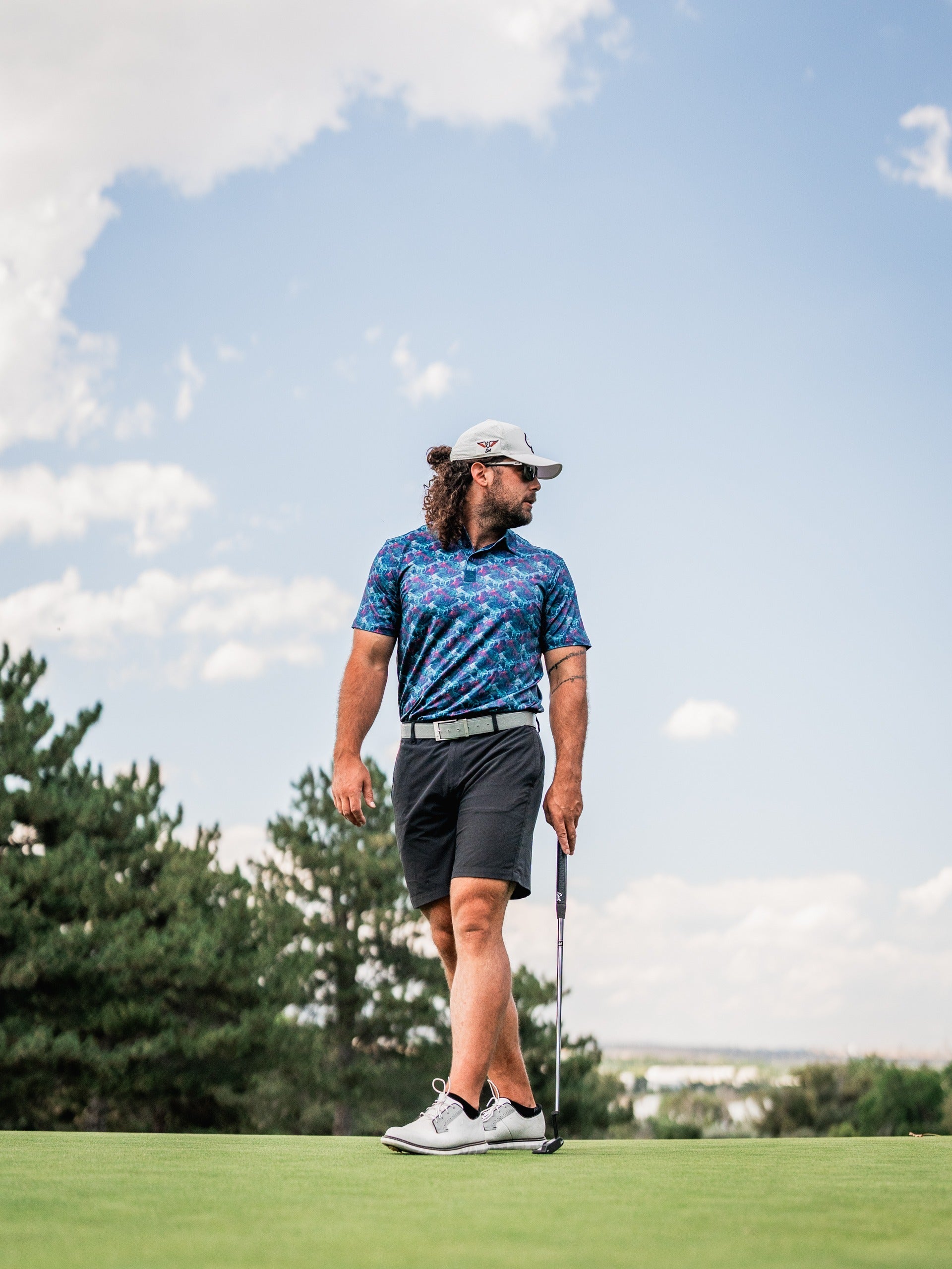 A golfer wearing a vibrant Swordfish Skelly polo and shorts stands confidently on the green, ready to putt.