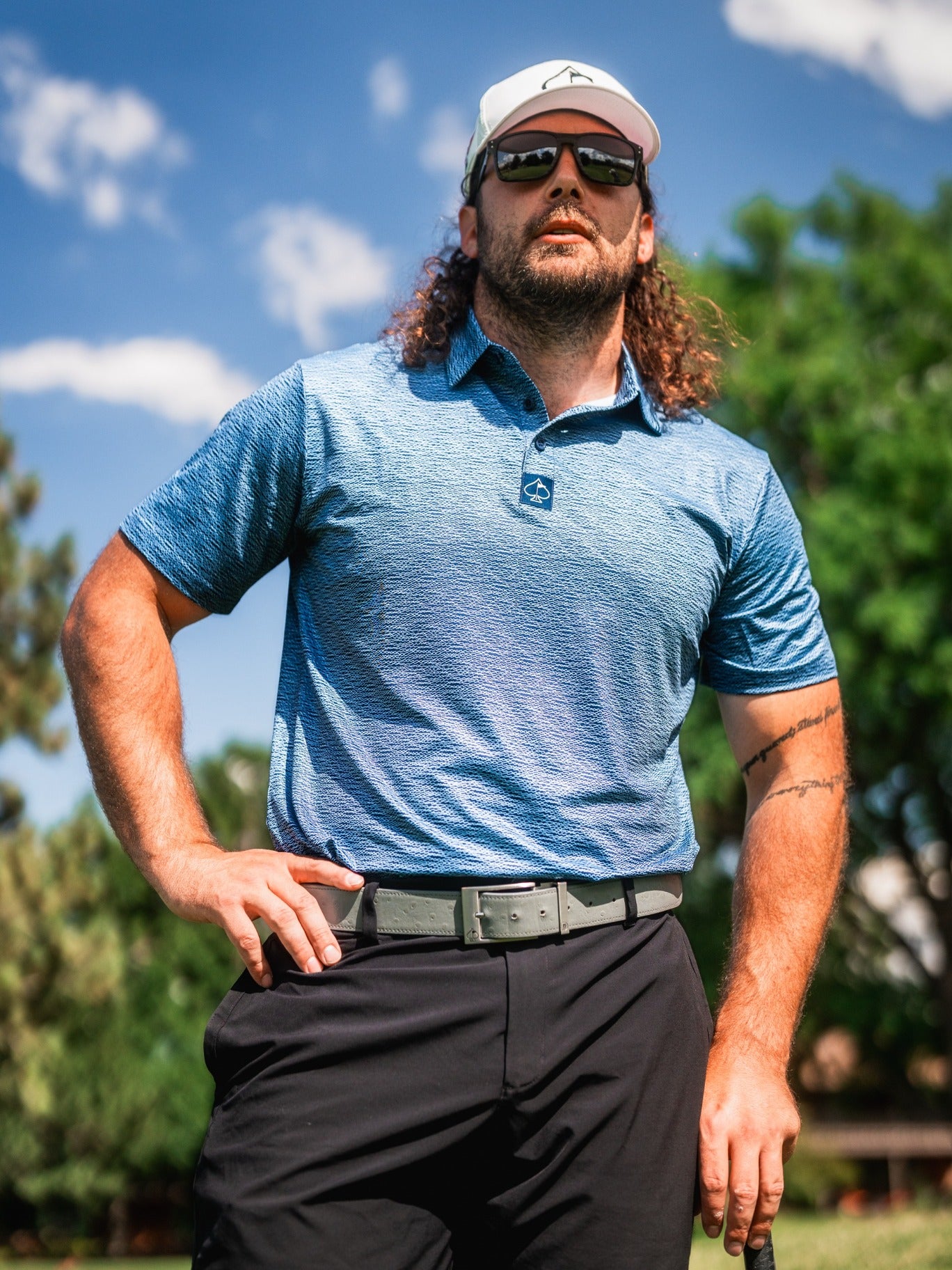 Bold blue golf polo with a textured squiggle pattern, worn by a man outdoors, showcasing a confident stance.