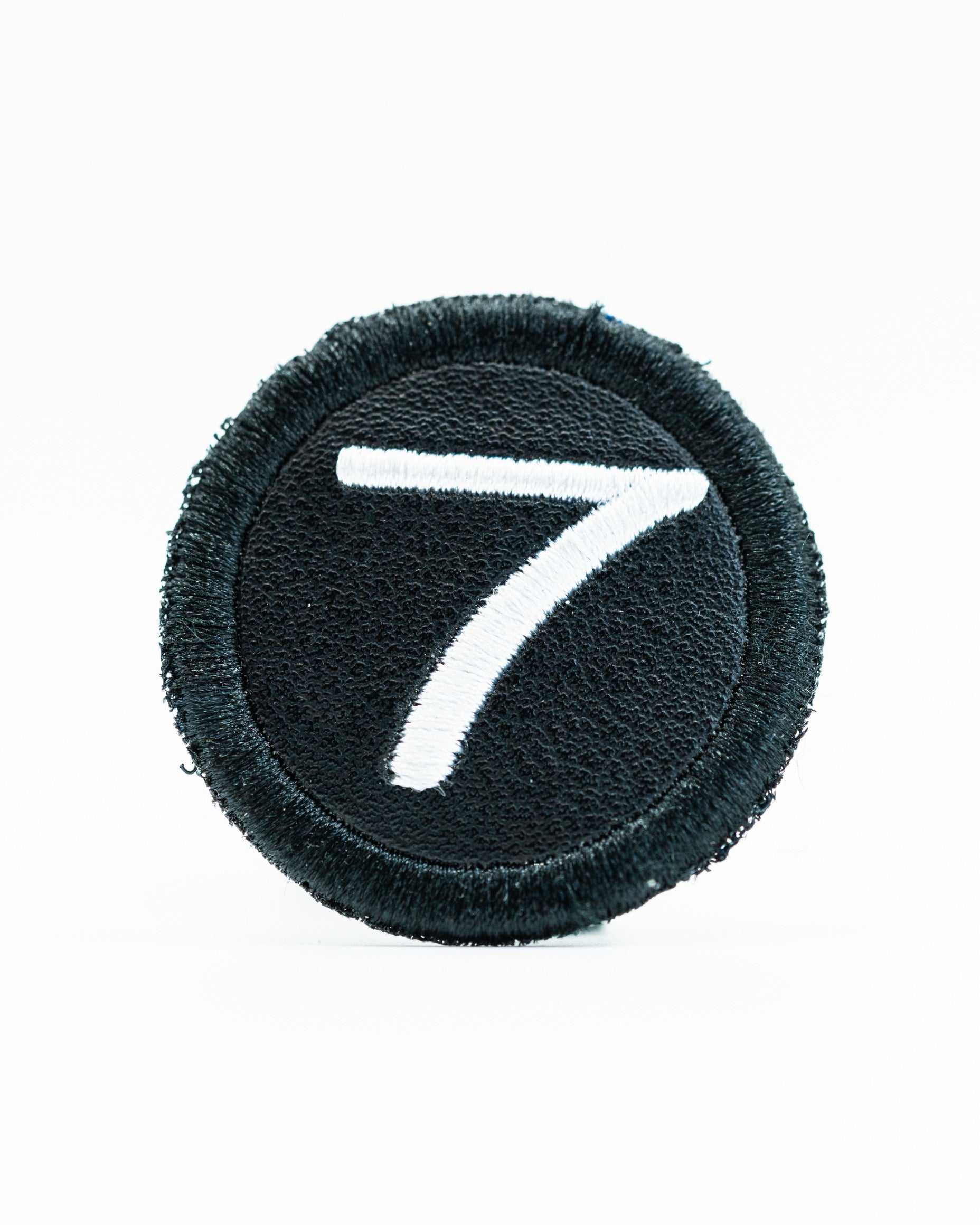 Black headcover patch featuring a white embroidered number seven, designed for personalized golf accessories.