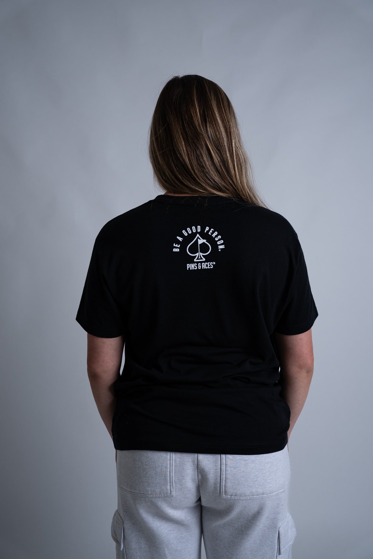Black Be A Good Person X Pins and Aces signature t-shirt featuring a logo on the back, designed for stylish golfers.