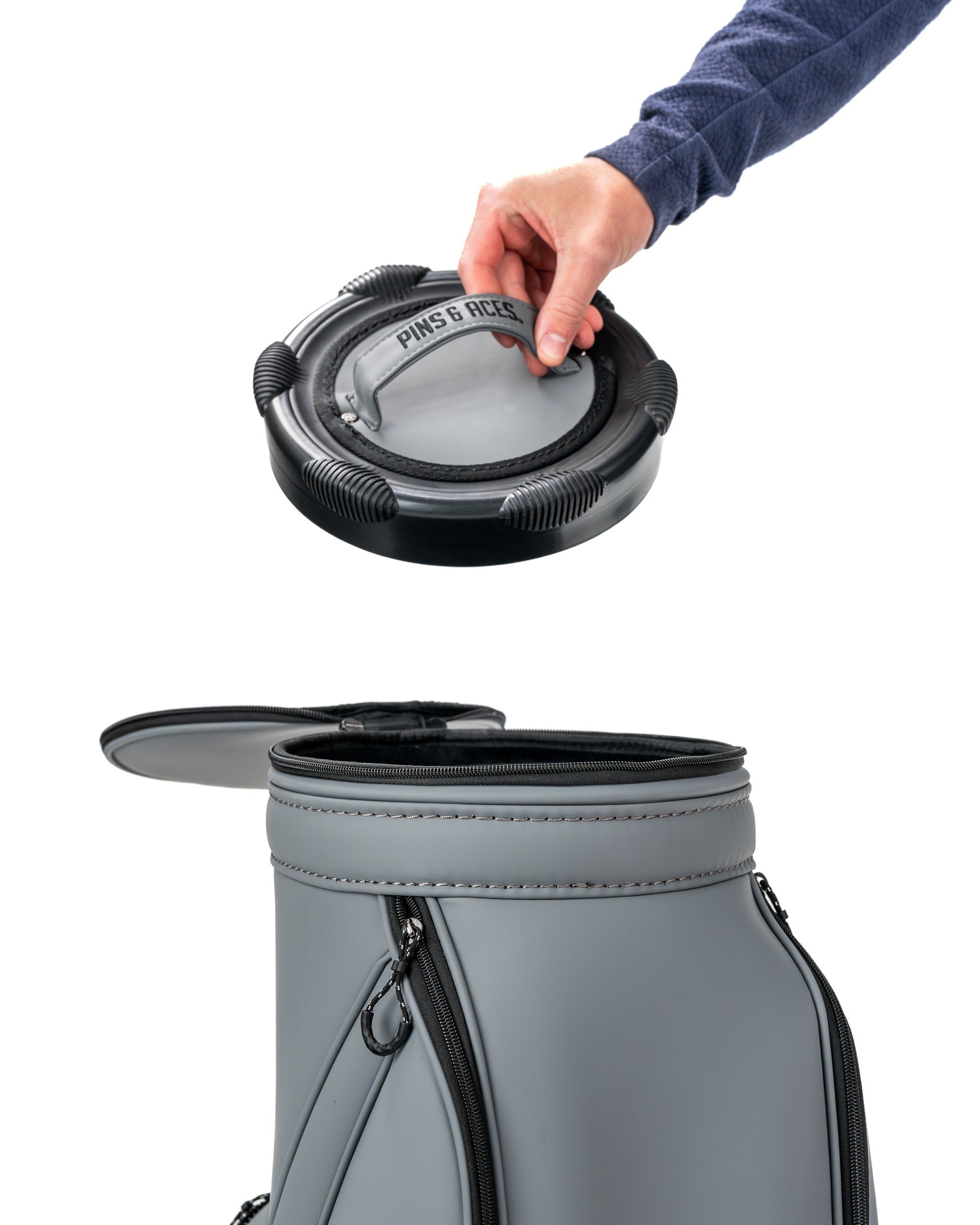 A person placing a flat ash Den Caddy into a stylish gray golf bag, showcasing its sleek design and functionality.