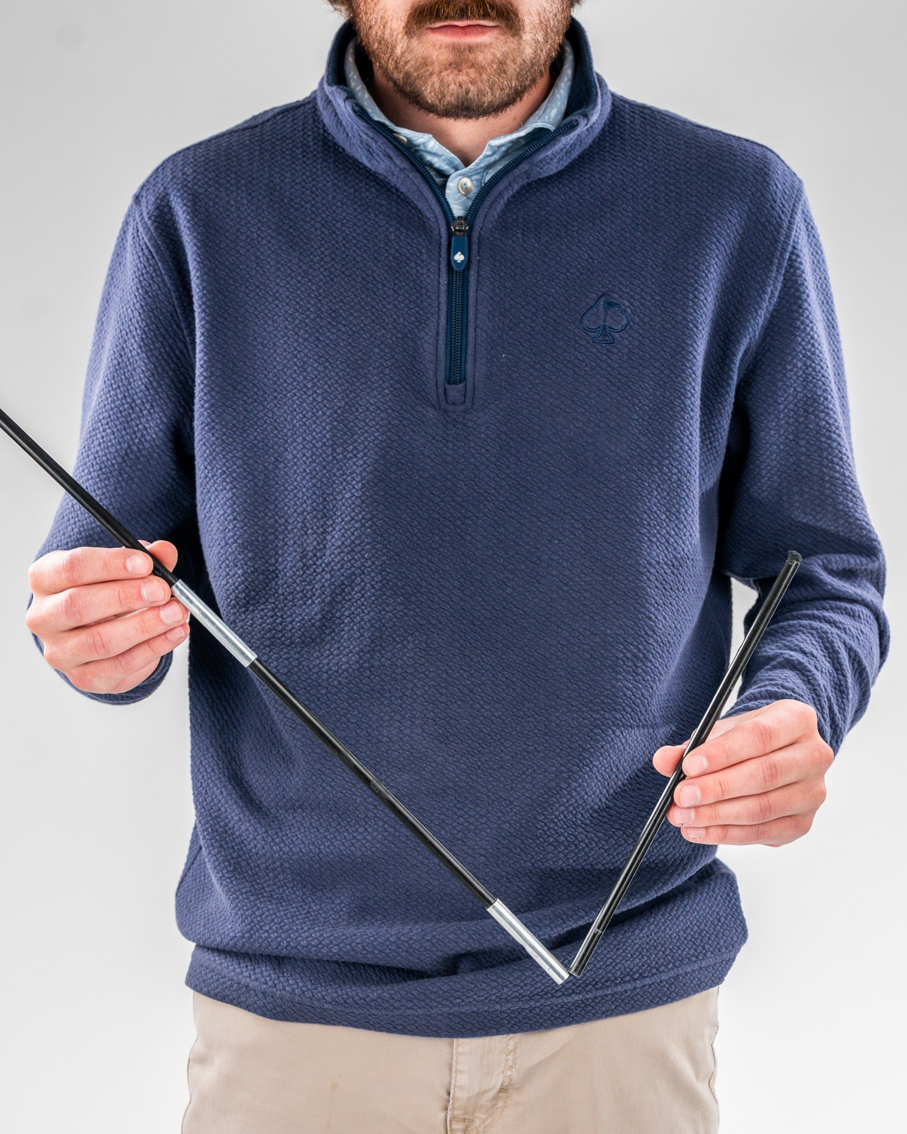 A golfer holding two golf clubs, wearing a navy quarter-zip pullover, showcasing a stylish Sunday golf bag.