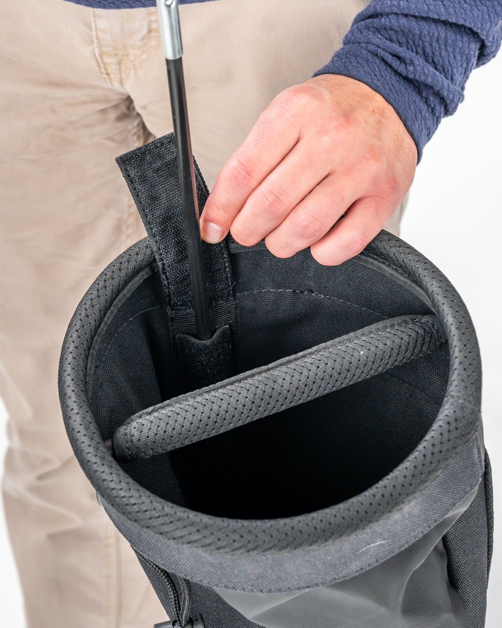 Close-up of a person inserting a golf club into a Sunday golf bag, showcasing its spacious interior and durable design.
