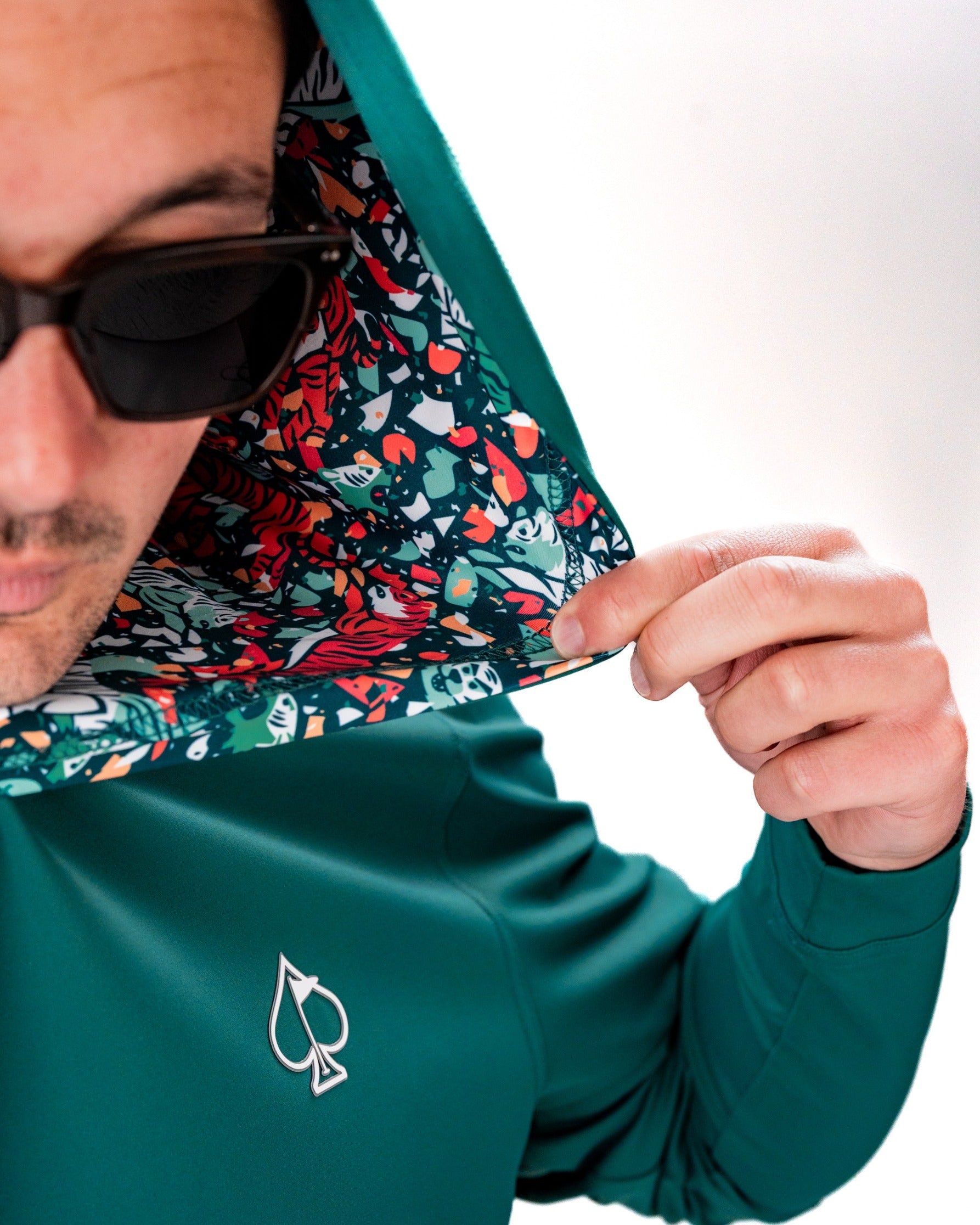 Performance golf hoodie in teal featuring a vibrant patterned hood and logo, ideal for stylish golfers on the course.