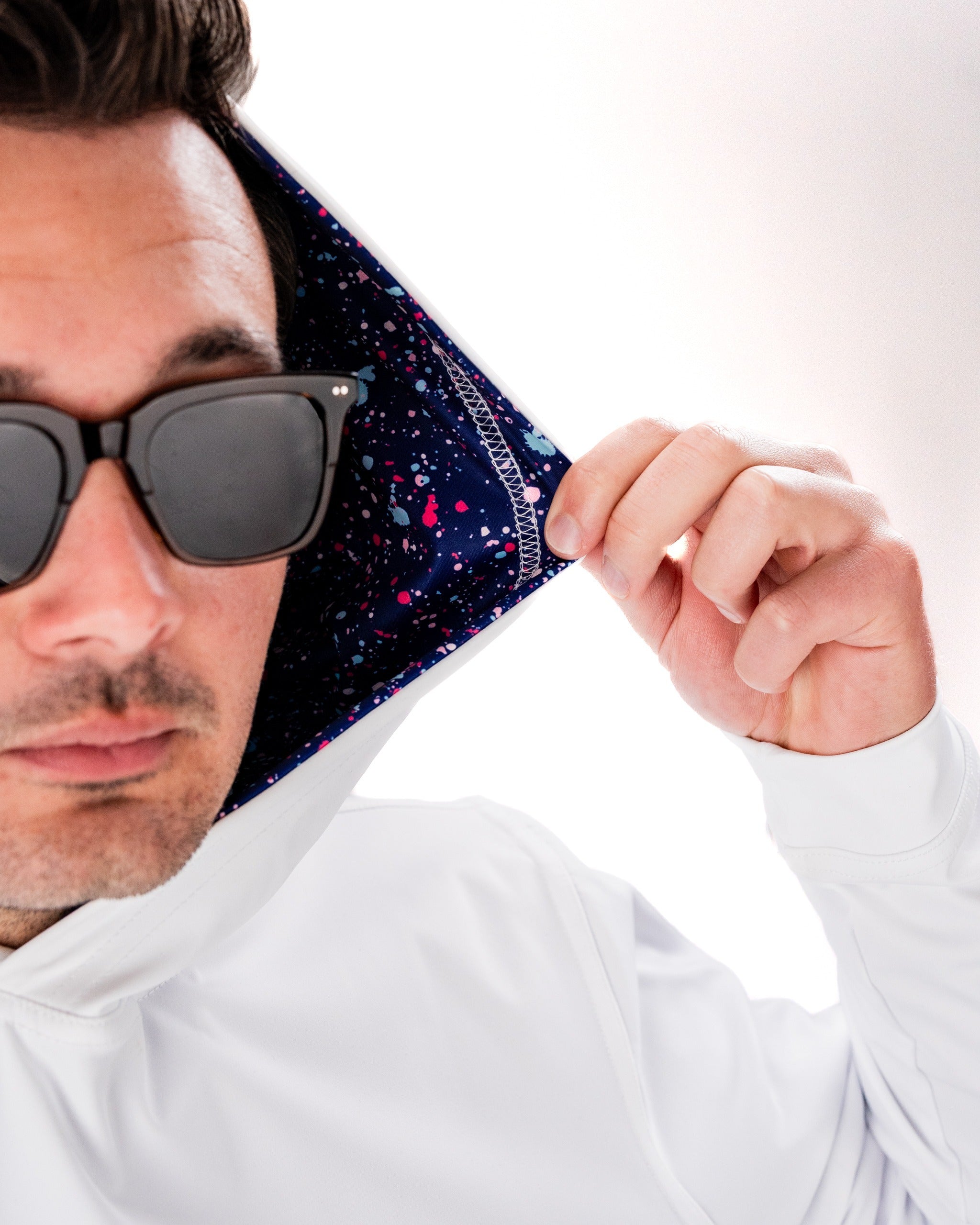 Man wearing a white performance golf hoodie, showcasing a blue splatter design on the inside of the hood.