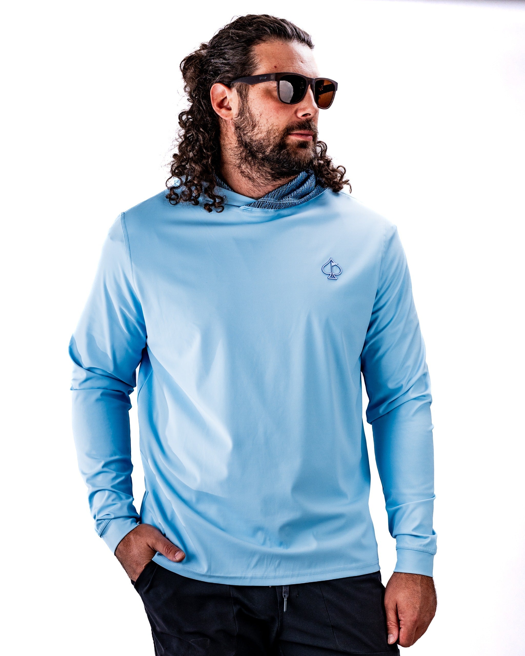 Man wearing a light blue performance golf hoodie with a hood and logo, styled with sunglasses against a white background.