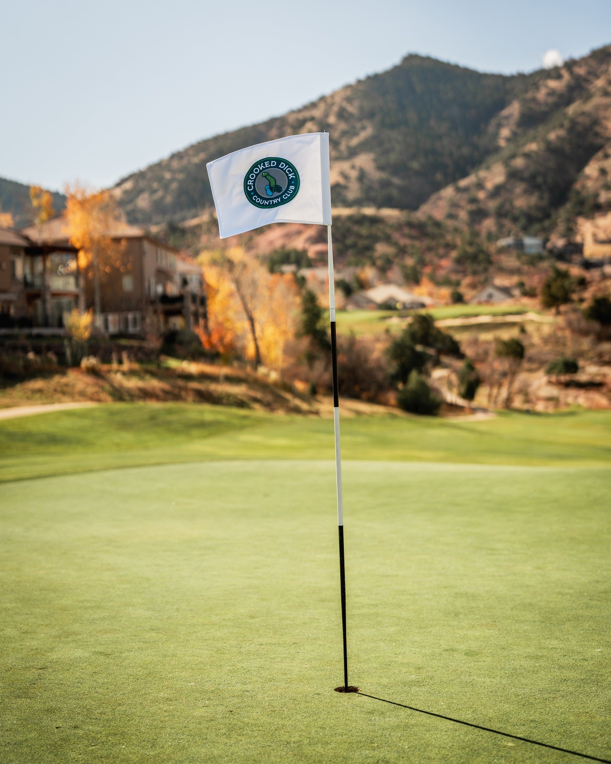 Crooked Dick golf flag on a green course with mountains in the background, showcasing a unique design for golfers.