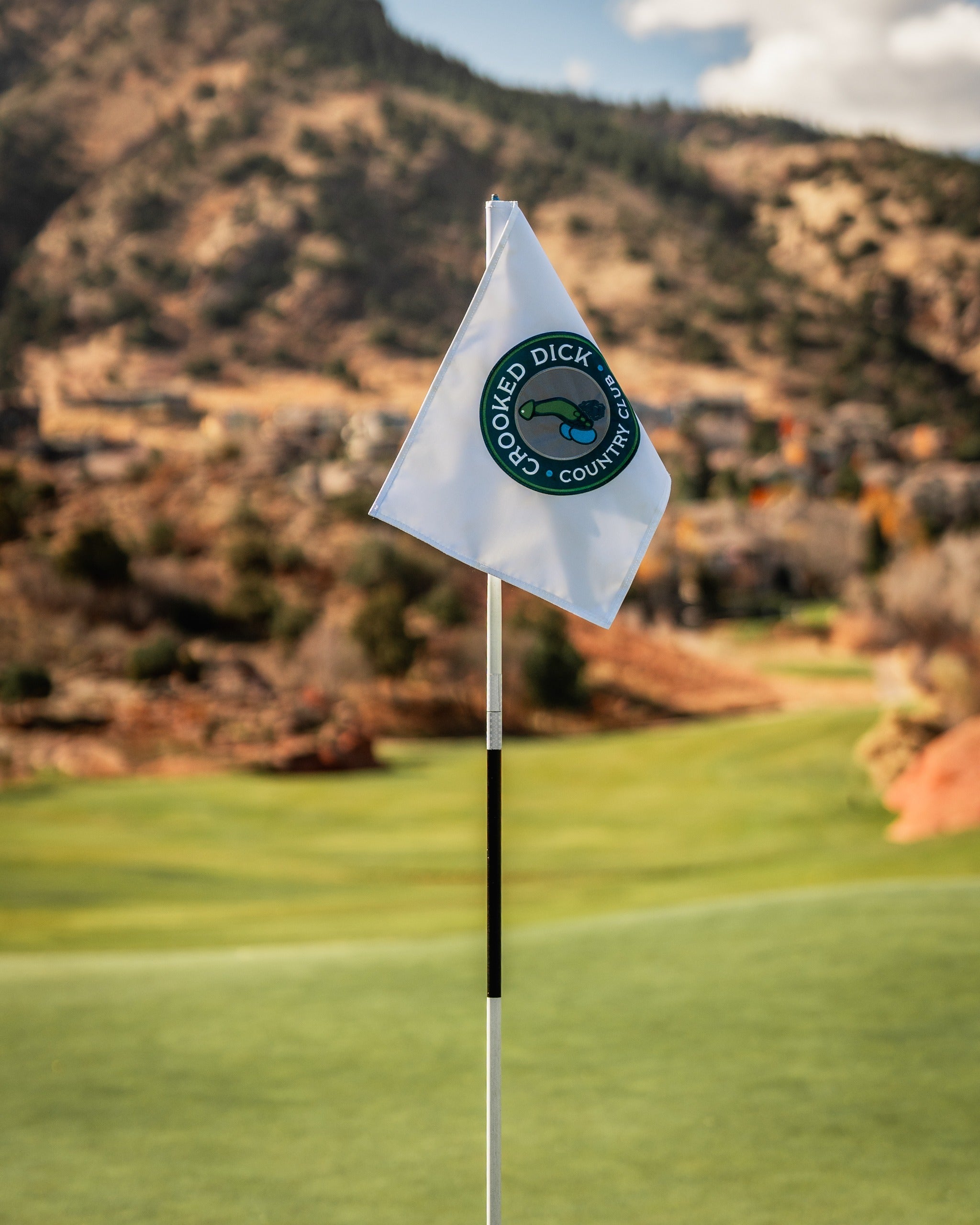 Crooked Dick golf flag featuring a circular logo, set against a scenic golf course backdrop.