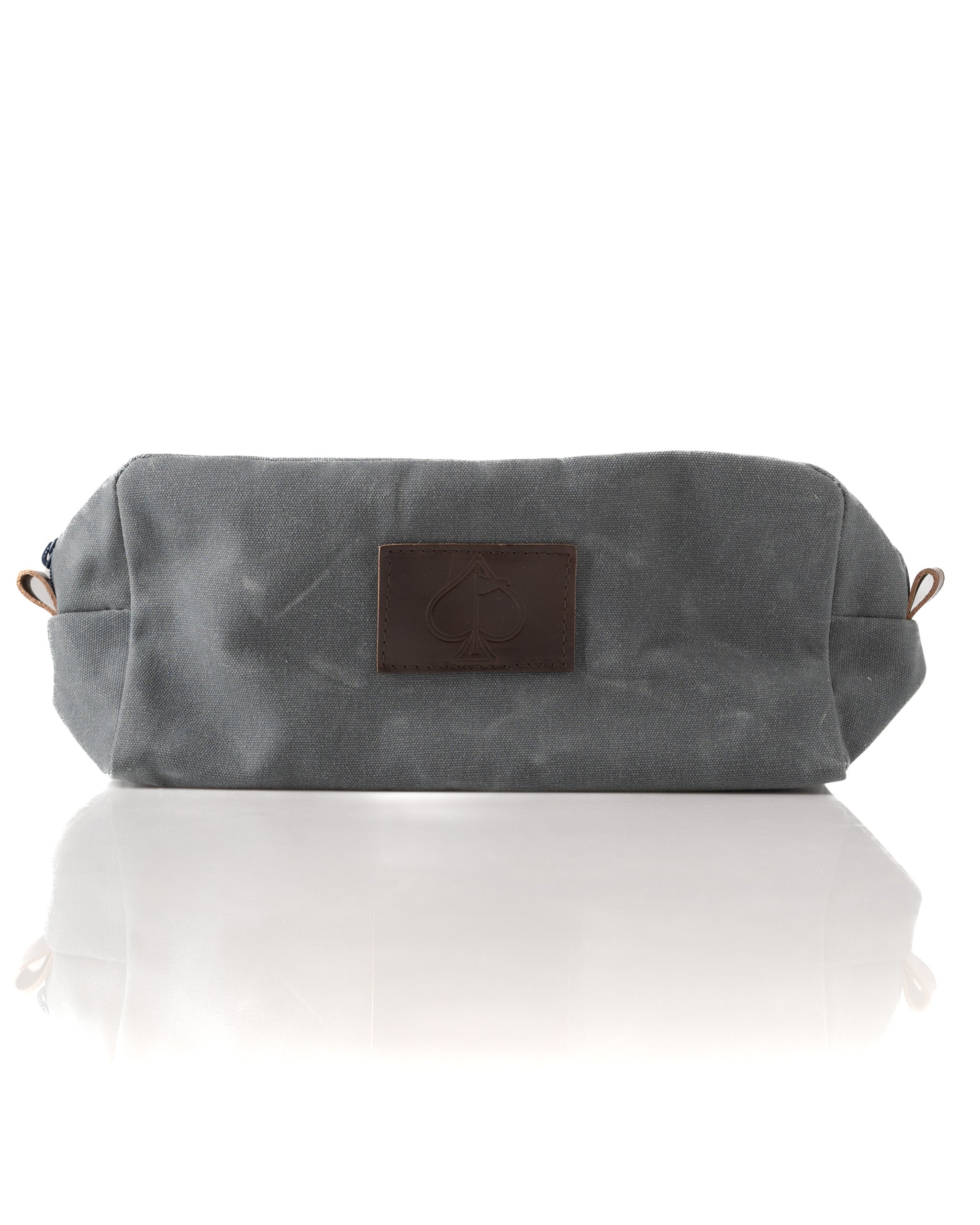 Gray toiletry bag with a leather logo patch, featuring a spacious design and a sleek, modern look.