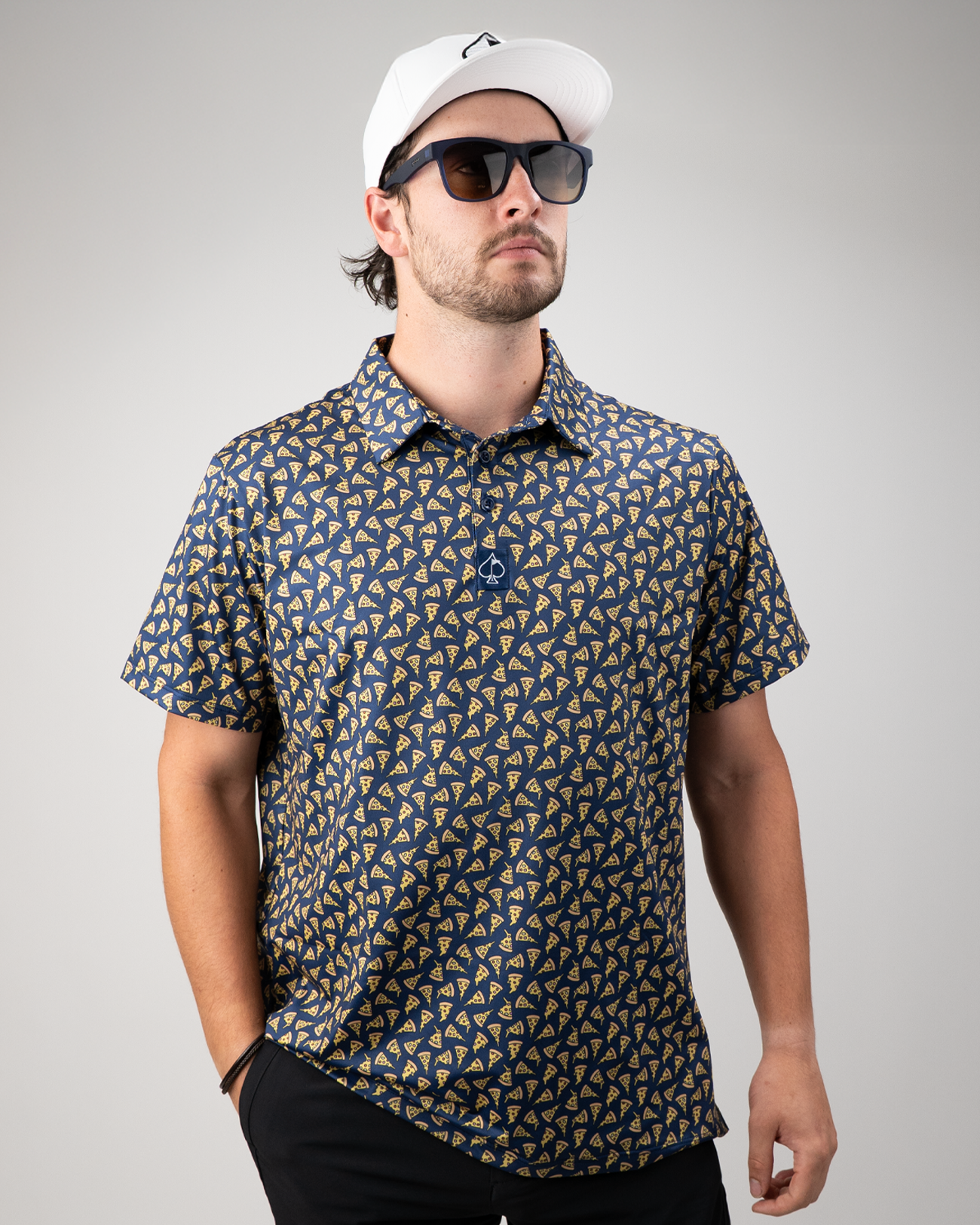 A golfer models a stylish pizza-patterned polo shirt, paired with sunglasses and a cap, showcasing bold golf fashion.