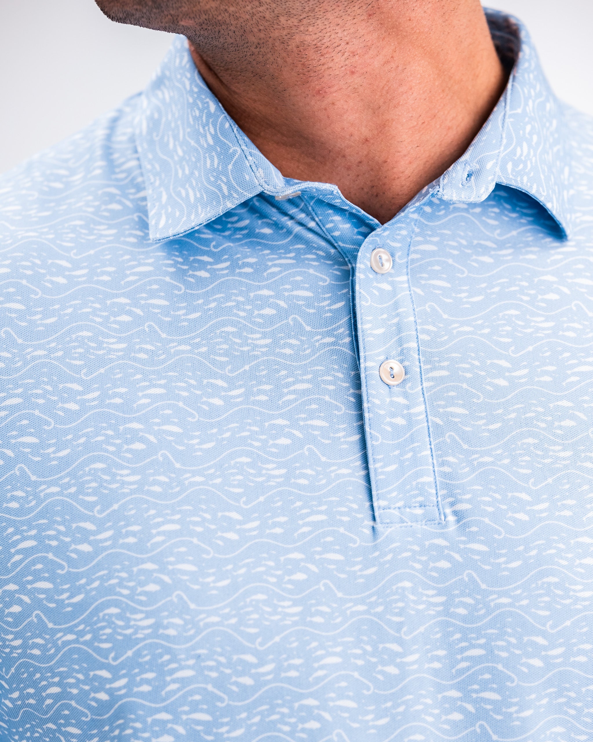 Close-up of a light blue golf shirt with white wave-like patterns, collar, and buttons, perfect for bold golf apparel.