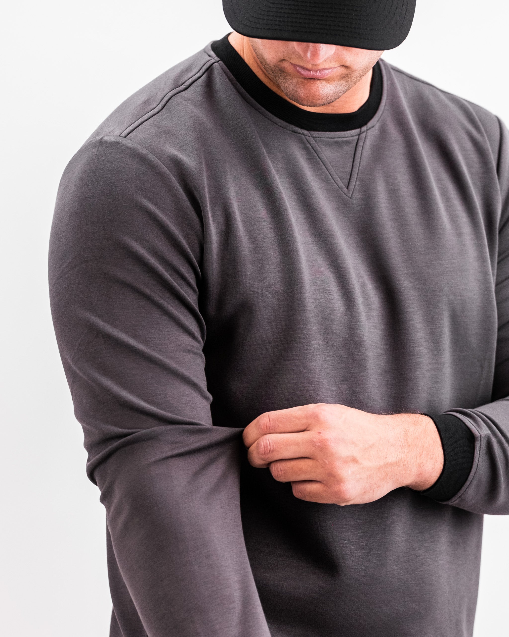 Close-up of a man wearing a slate grey Player Preferred™ Crewneck, adjusting his sleeve, with a black cap and black collar.
