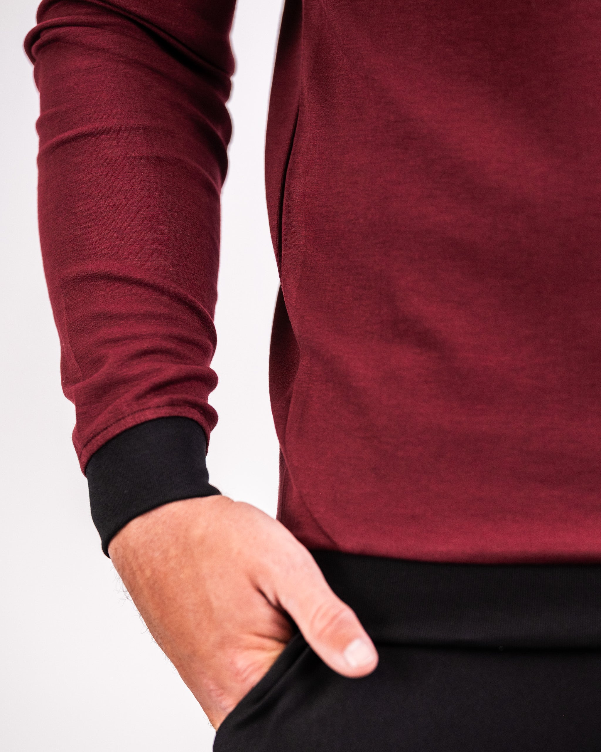 Close-up of a person wearing a maroon Player Preferred™ Crewneck with black cuffs, standing with one hand in their pocket.