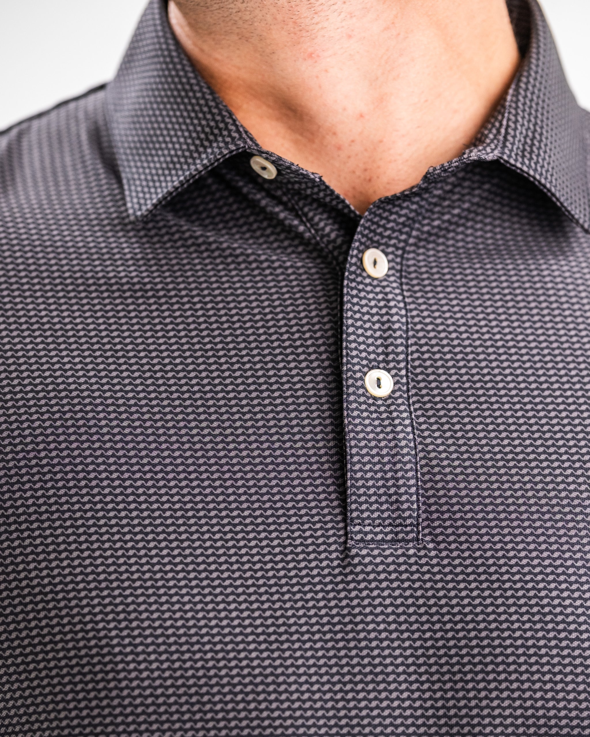 Close-up of a men's golf shirt with a dark, geometric pattern, white buttons, and a classic collar for bold golf style.
