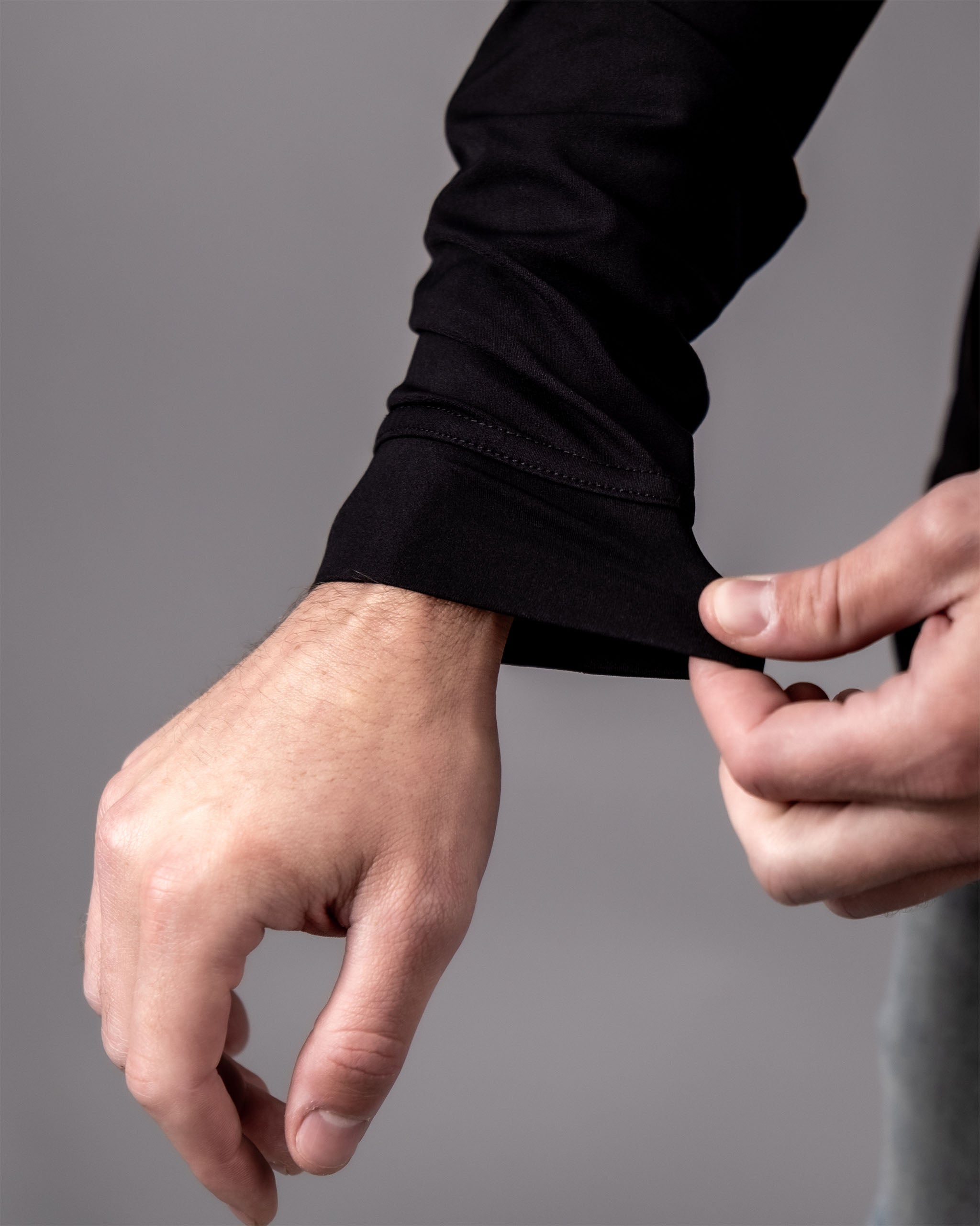 Close-up of a person adjusting the cuff of a black performance golf hoodie with a poker design, showing the fabric and stitching details.