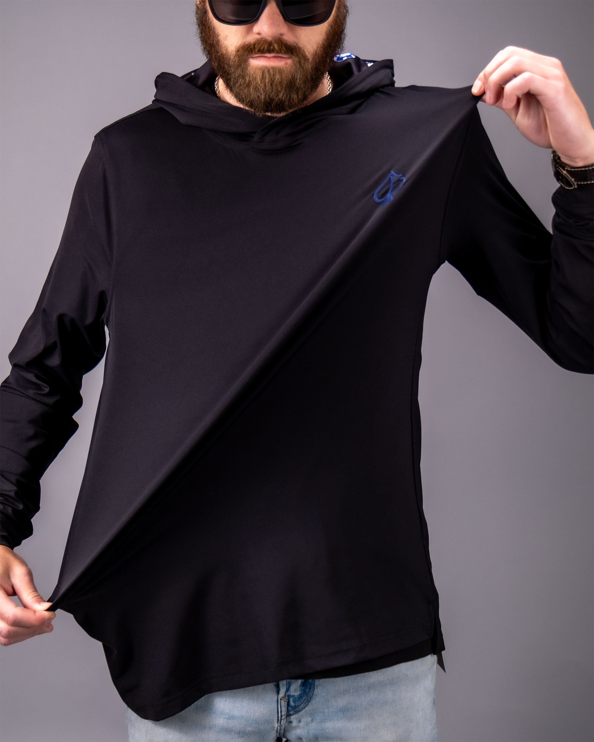 Man wearing a black performance golf hoodie with a subtle blue logo, demonstrating its lightweight, flexible fabric.