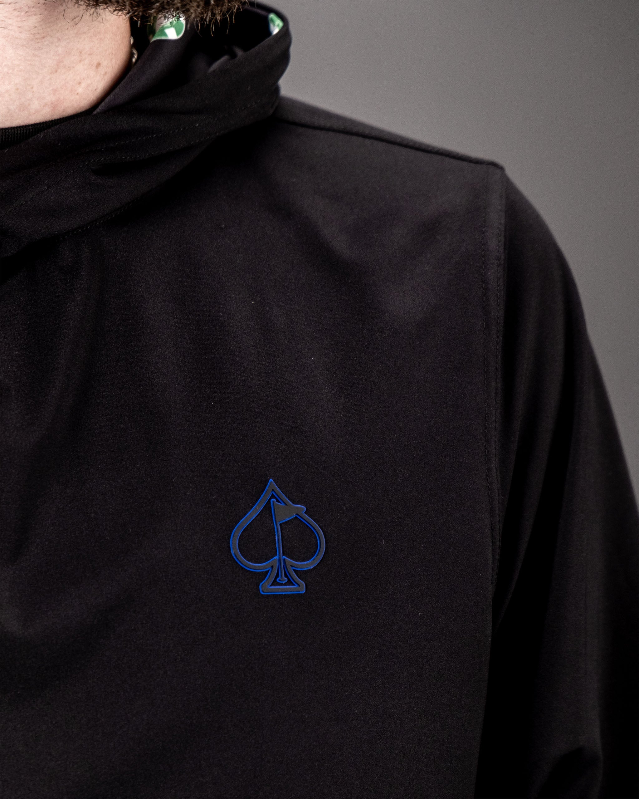 Black performance golf hoodie with a blue spade logo on the chest, designed for comfort and style during golf activities.
