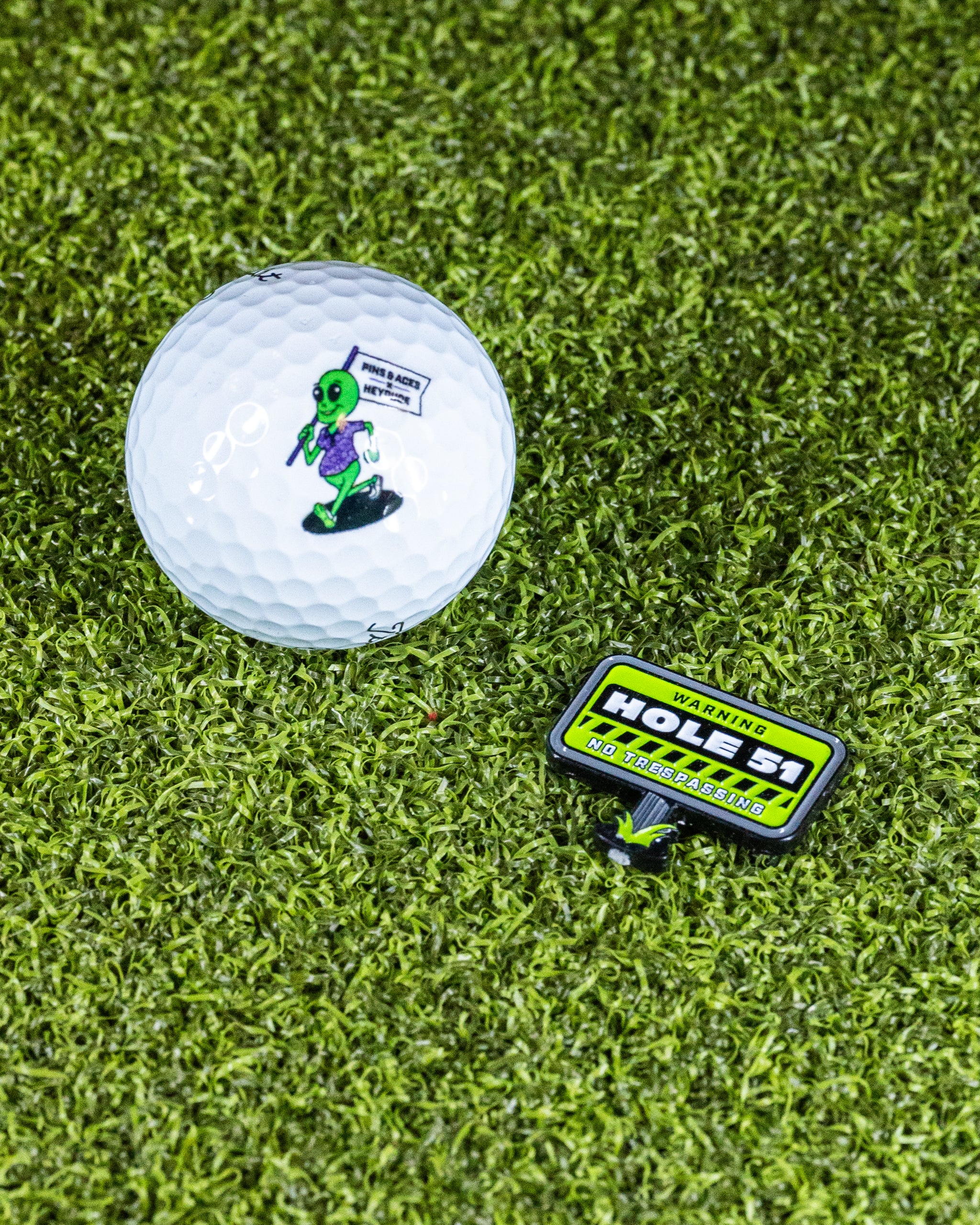 HEYDUDE Hole 51 Ball Marker featuring a circular design with vibrant colors and the HEYDUDE logo. Perfect for golf enthusiasts.