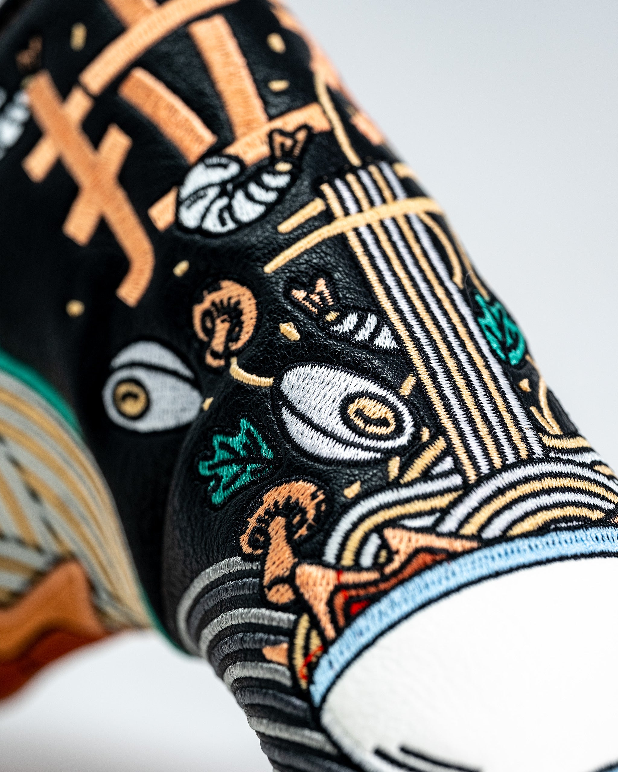 Close-up of a black embroidered Blade Putter Cover featuring colorful sushi and ramen bowl designs with detailed stitching.