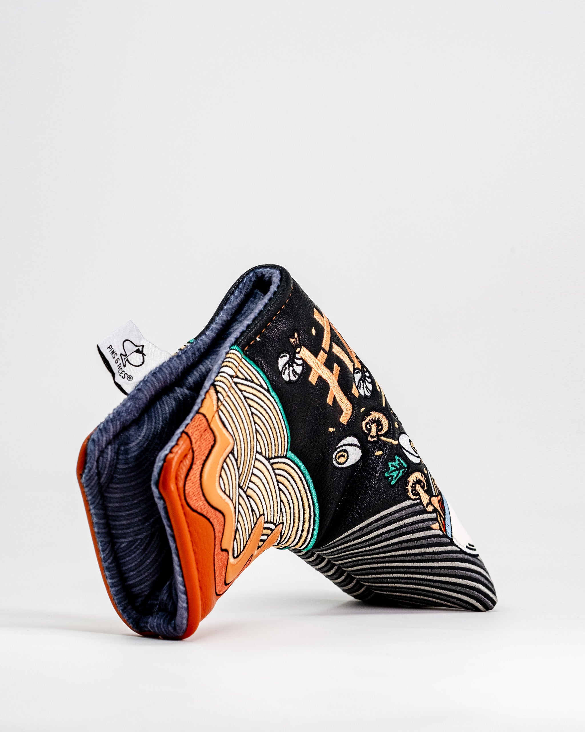 Colorful ramen bowl design Blade Putter Cover with embroidered details, black background, and striped interior lining.