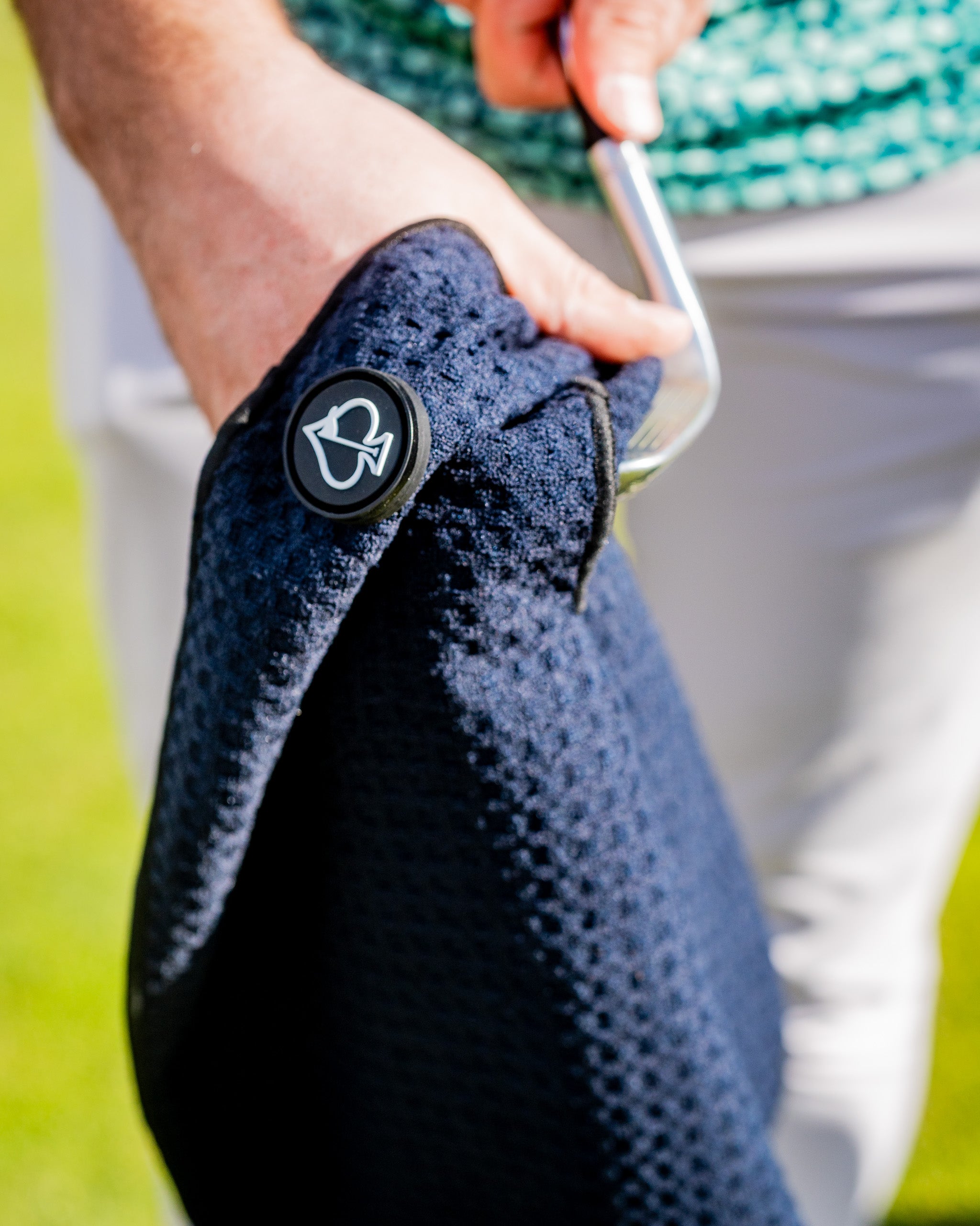 Close-up of a navy textured golf glove with a black logo button, held by a golfer with a putter, showcasing bold golf acce...