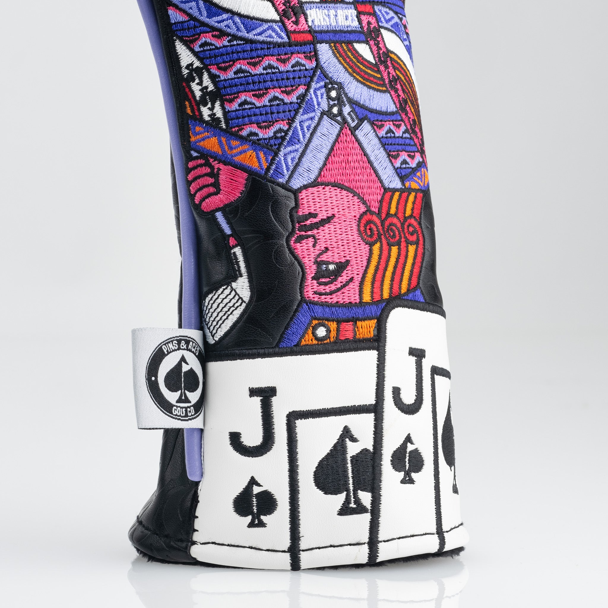 Colorful embroidered golf headcover with bold playing card and face designs, black, white, pink, purple, and orange accents.