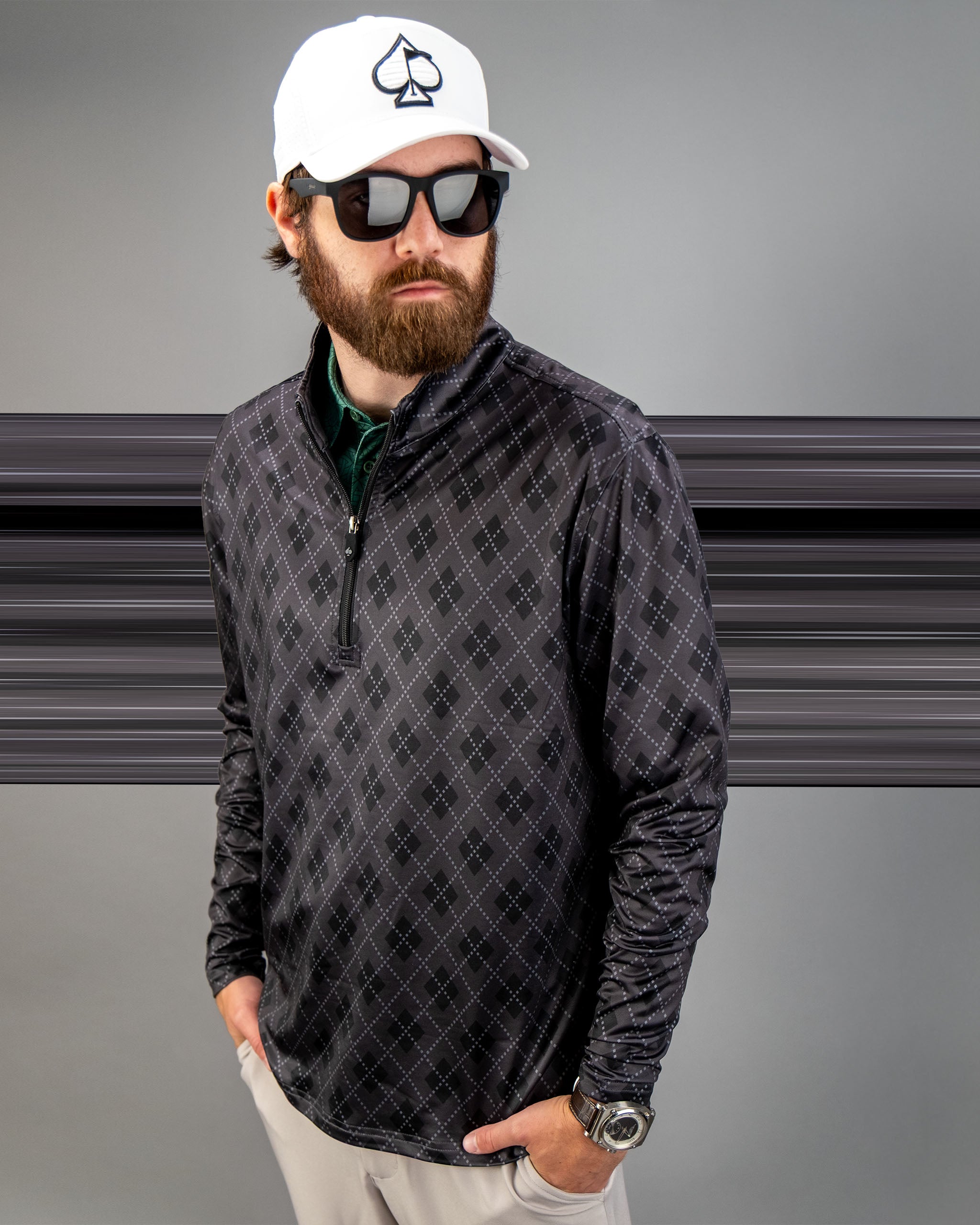 Man wearing a black London Fog pullover with a diamond pattern, sunglasses, and a white cap, posing confidently.