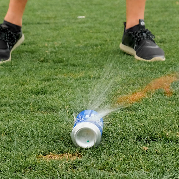 Colorful golf headcover with bold blue, white, and teal design, shot mid-fall on lush green grass with a spray of water.