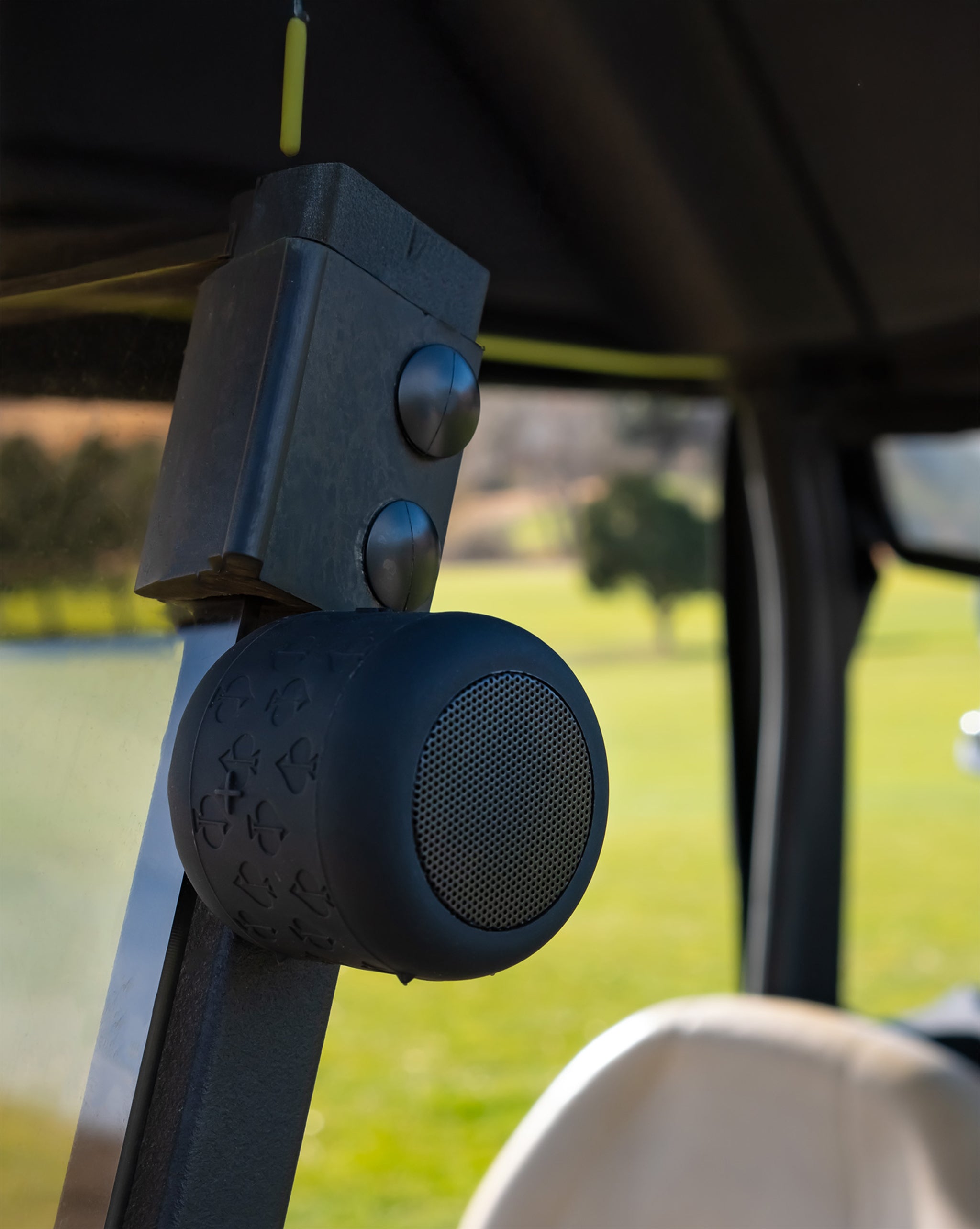 Close-up of a black portable speaker mounted inside a golf cart, with a metal bracket and a yellow string in the background.