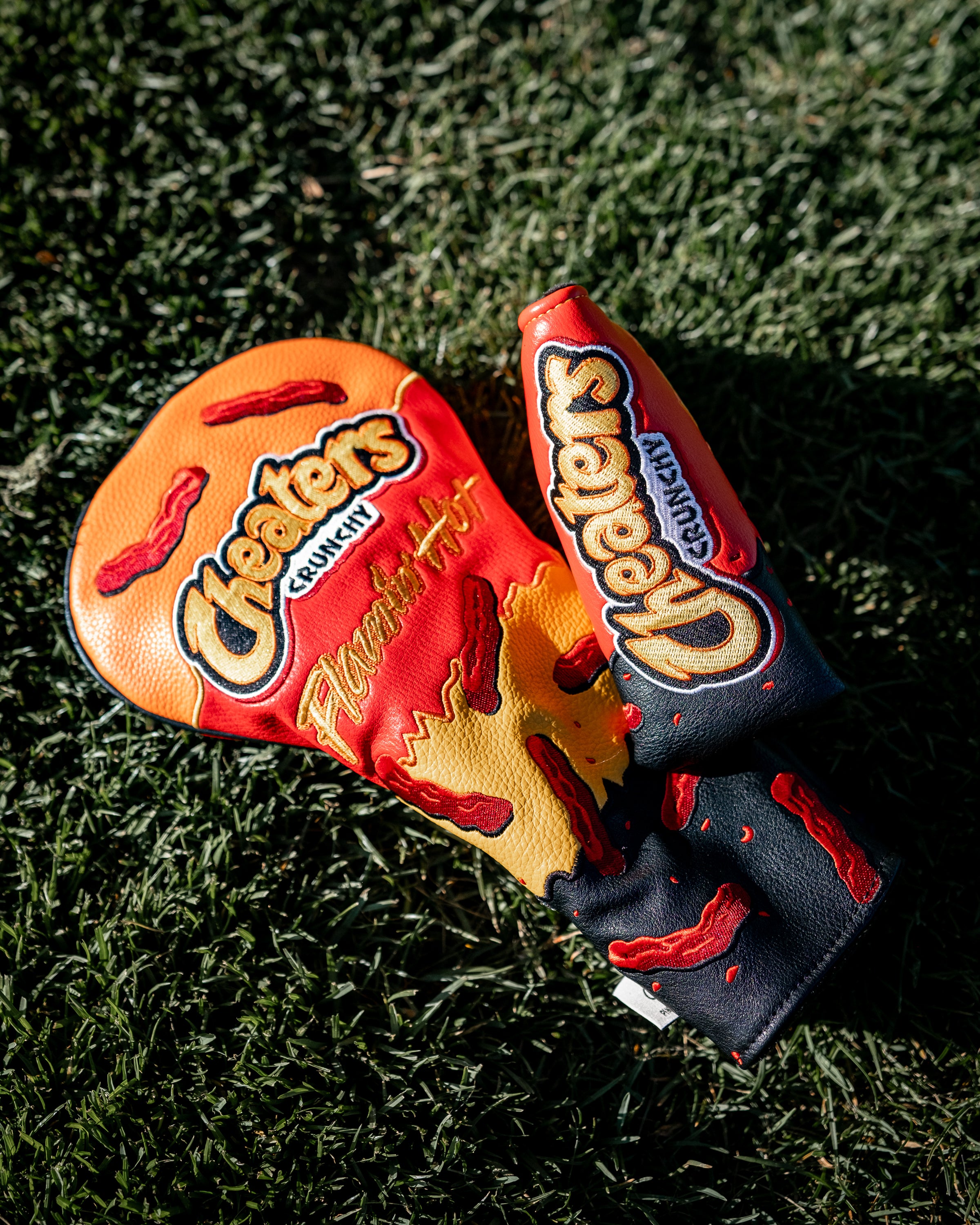 Cheater's Flamin' Hot Blade Putter Cover featuring bold chili pepper and fiery design on grass.