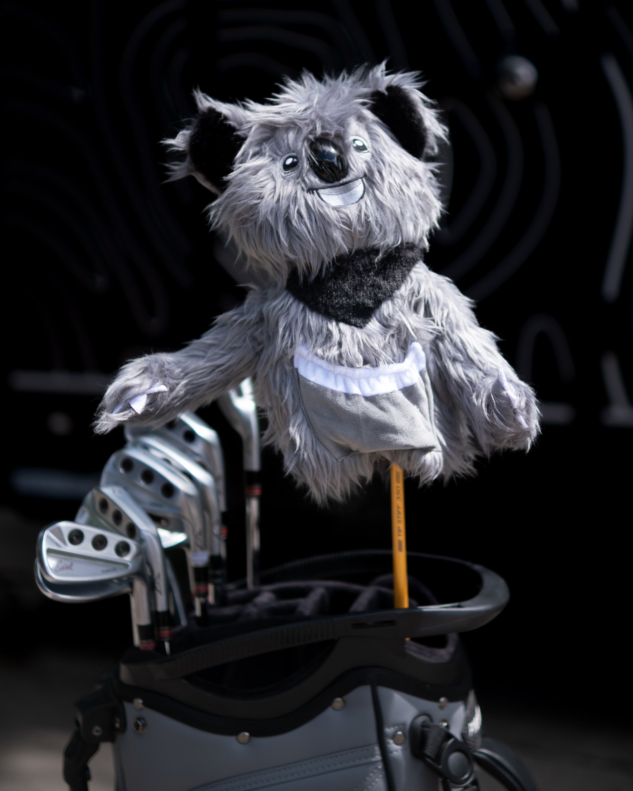 A plush koala-themed golf driver cover with a smiling face, fluffy gray fur, and black ears, attached to a golf bag.