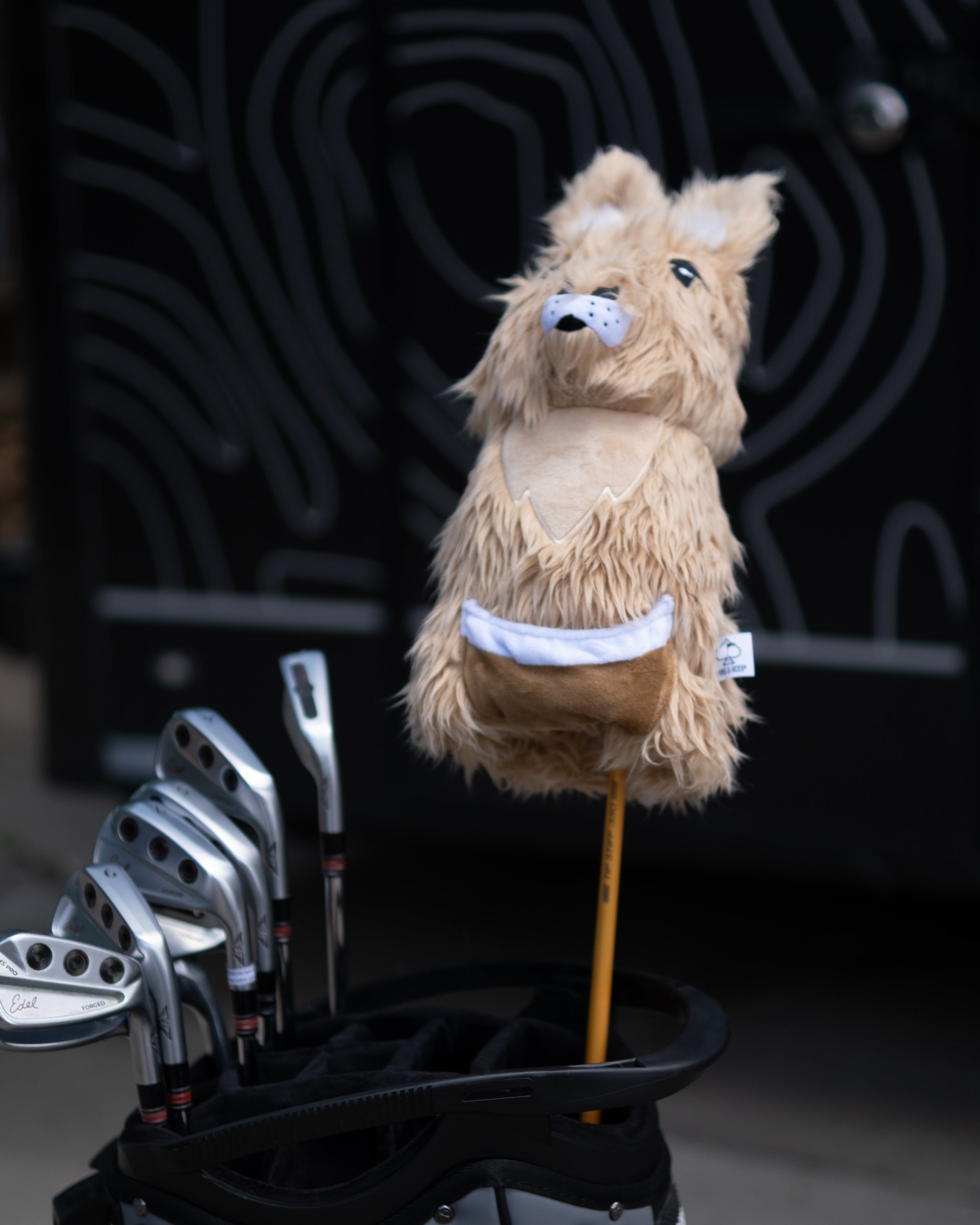 Golf club driver cover shaped like a kangaroo with a furry texture and a pouch, attached to a golf bag.