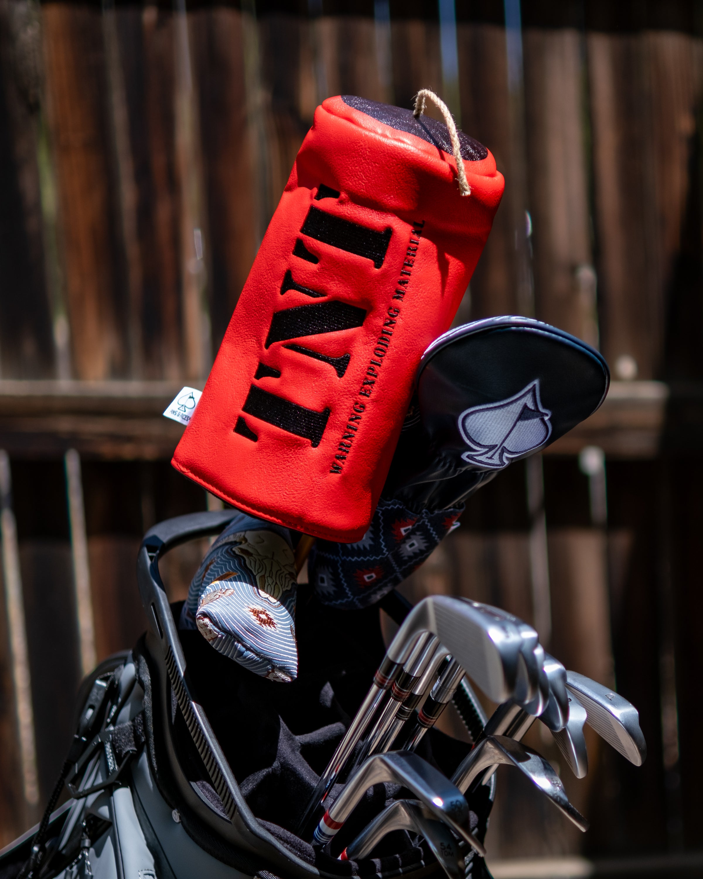 Red TNT driver golf club cover with black lettering, attached to a golf bag containing clubs and other accessories.