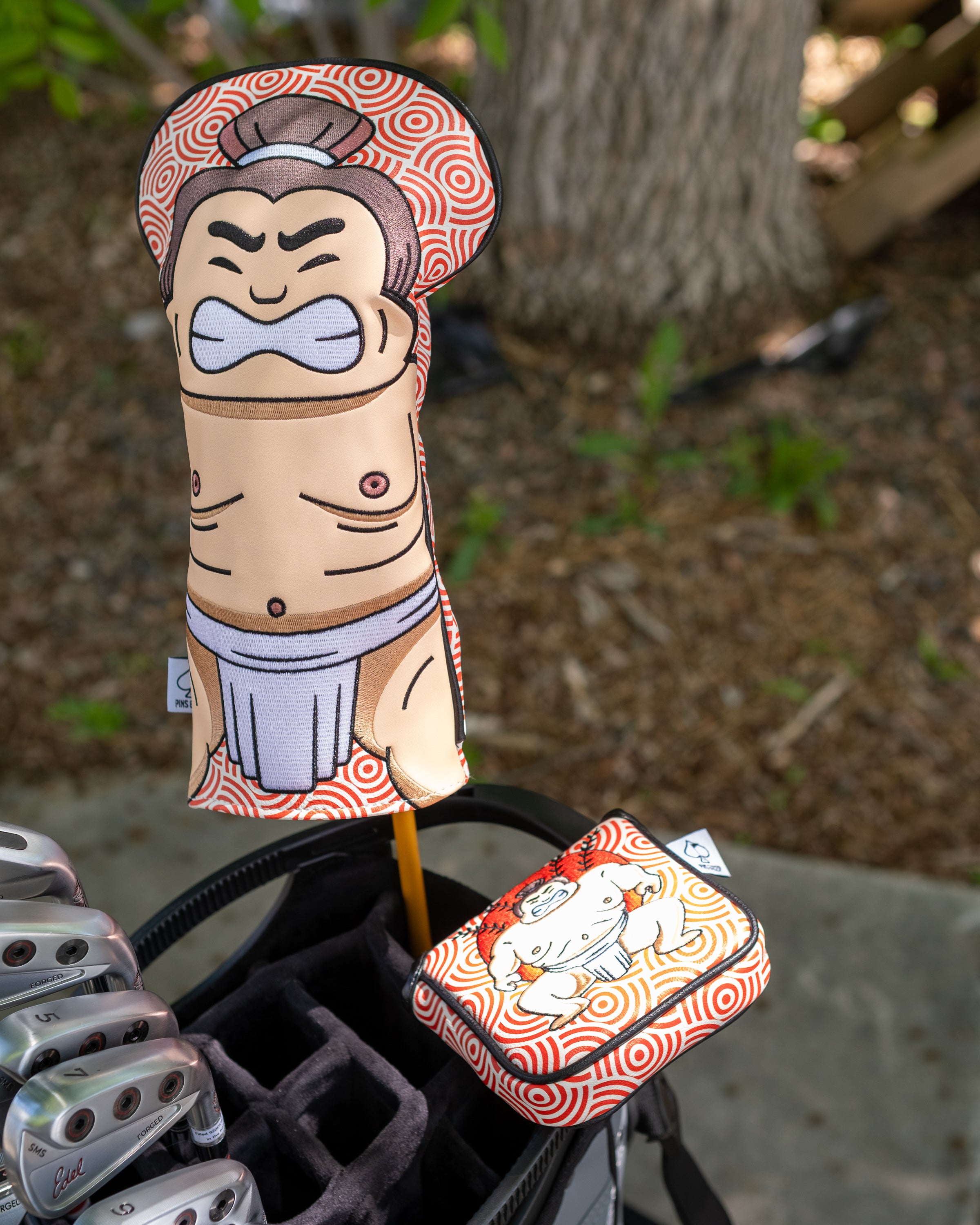 Sumo-themed golf driver and accessory covers with cartoon sumo wrestler designs, attached to a golf bag.
