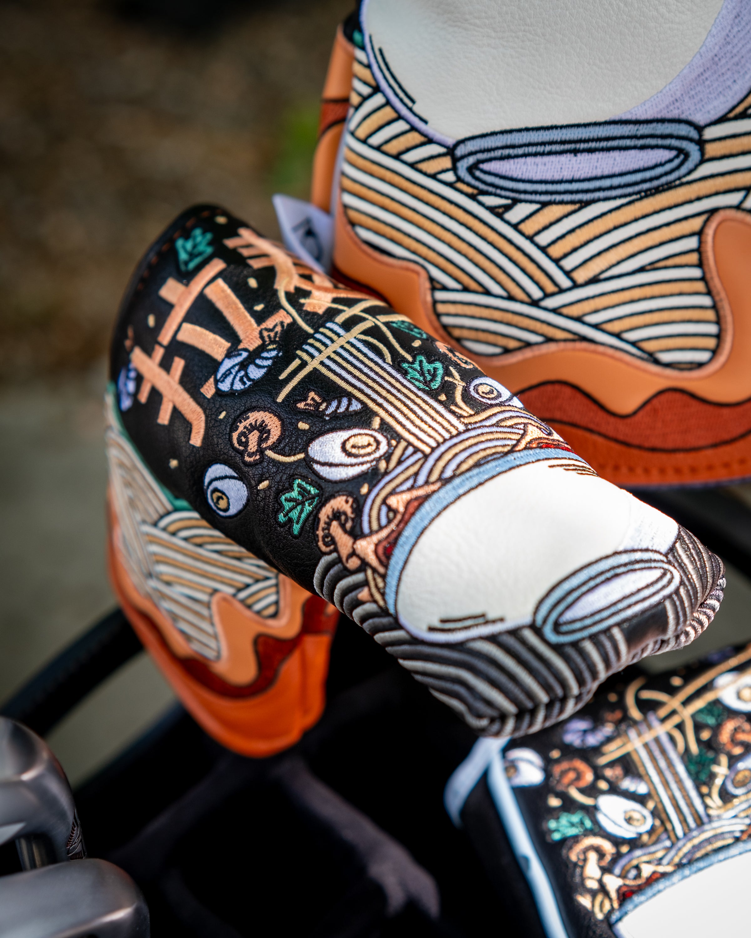 Colorful ramen bowl-shaped blade putter cover with embroidered details and vibrant patterns on golf club.