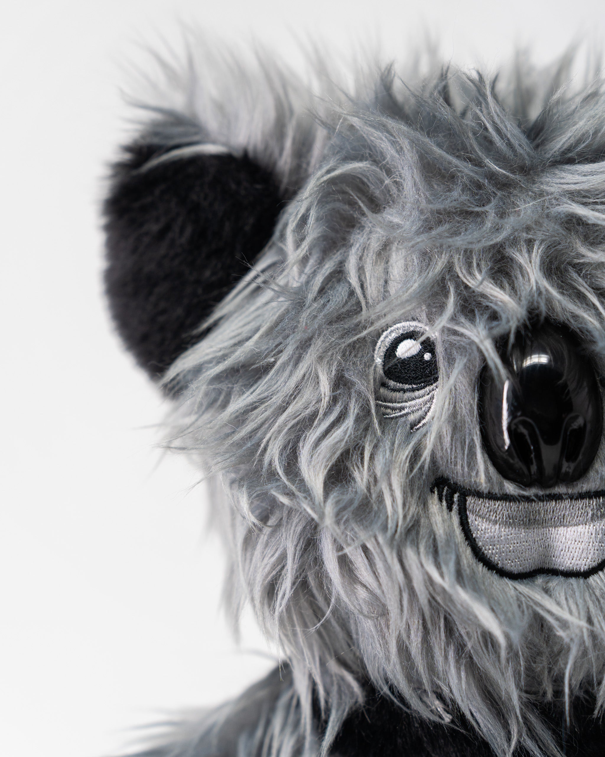 Close-up of a koala-themed driver cover with gray faux fur, embroidered eye, black nose, and smiling mouth, designed for golf clubs.