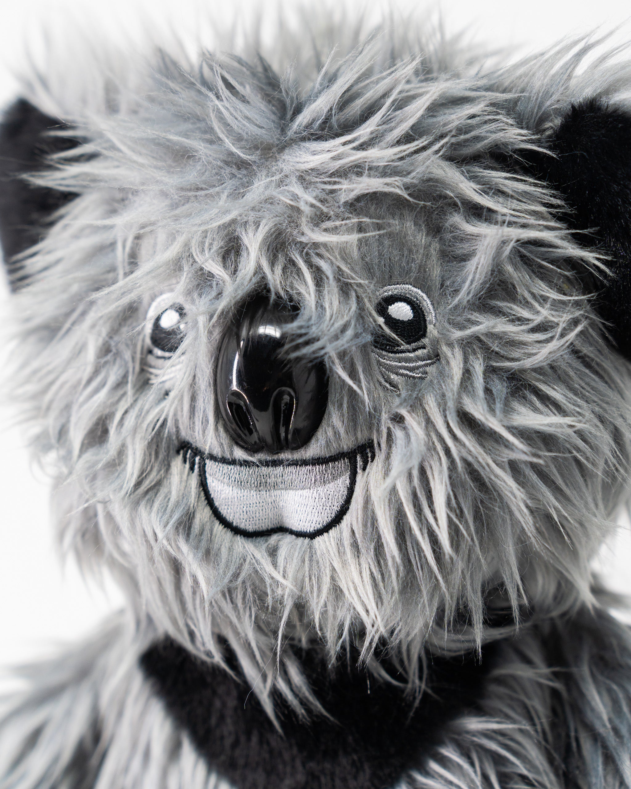 Close-up of a plush koala driver cover with detailed gray and black fur, shiny black nose, and embroidered smiling mouth.