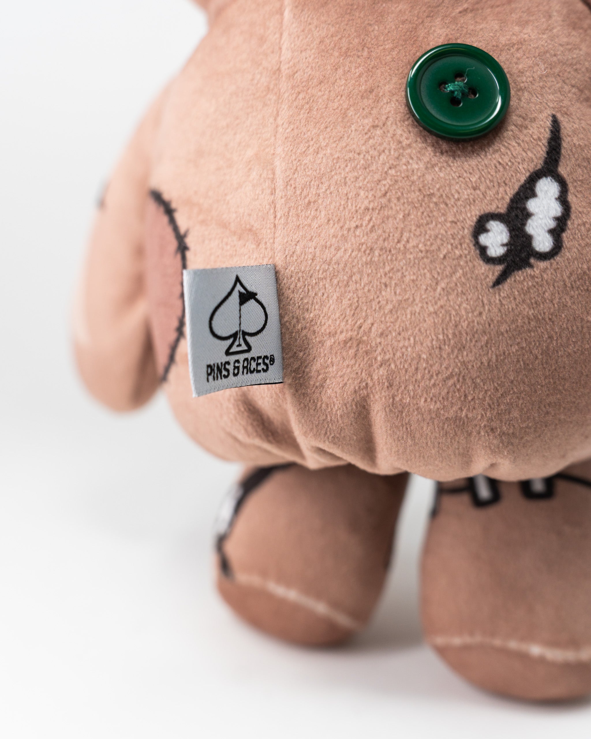 Close-up of a Pins and Aces Voodoo Doll driver cover with a pink fabric, green button, and embroidered black and white design.