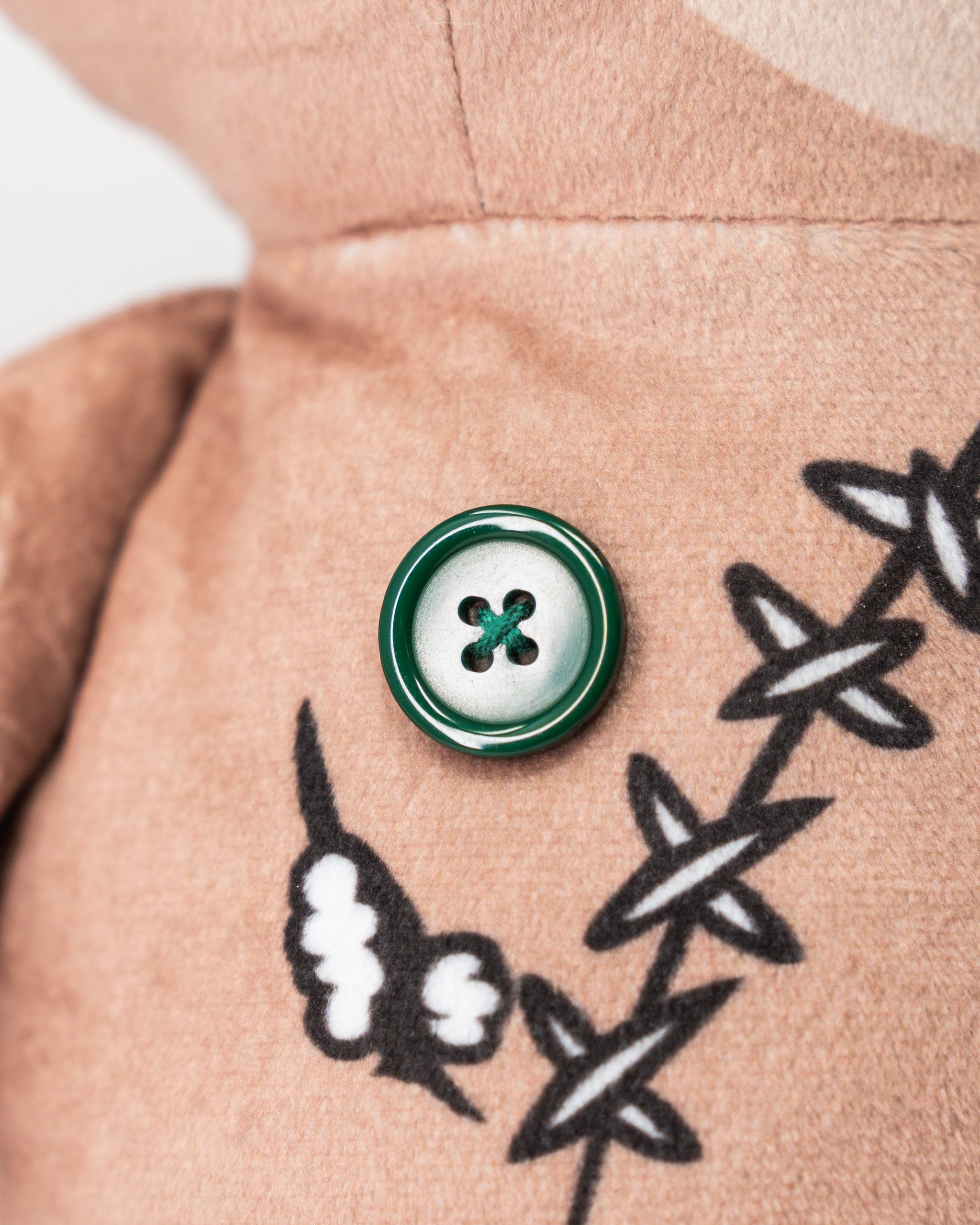 Close-up of a beige golf driver cover featuring a green and white button and a black and white embroidered voodoo doll design.