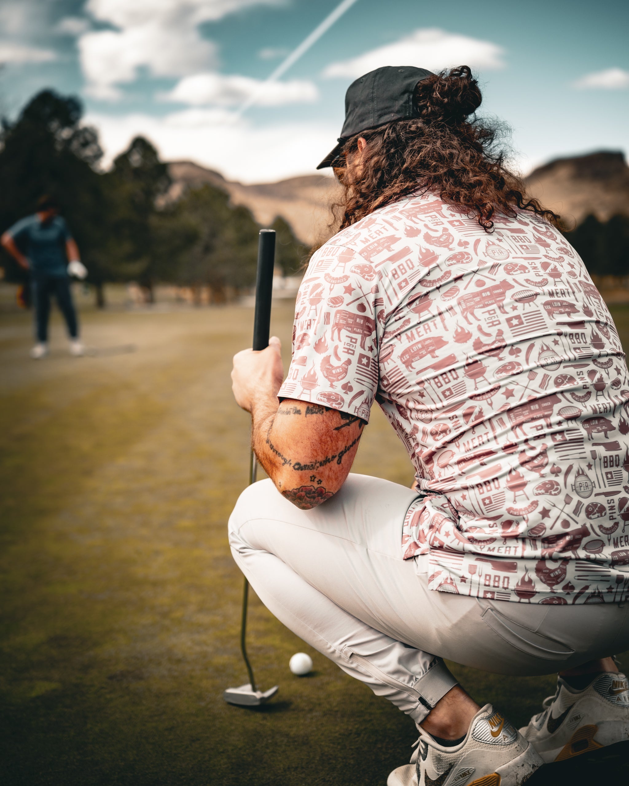 Tall, charcoal grey Pitmaster apron with pockets, being worn by a person grilling outdoors, surrounded by greenery and barbecue tools.