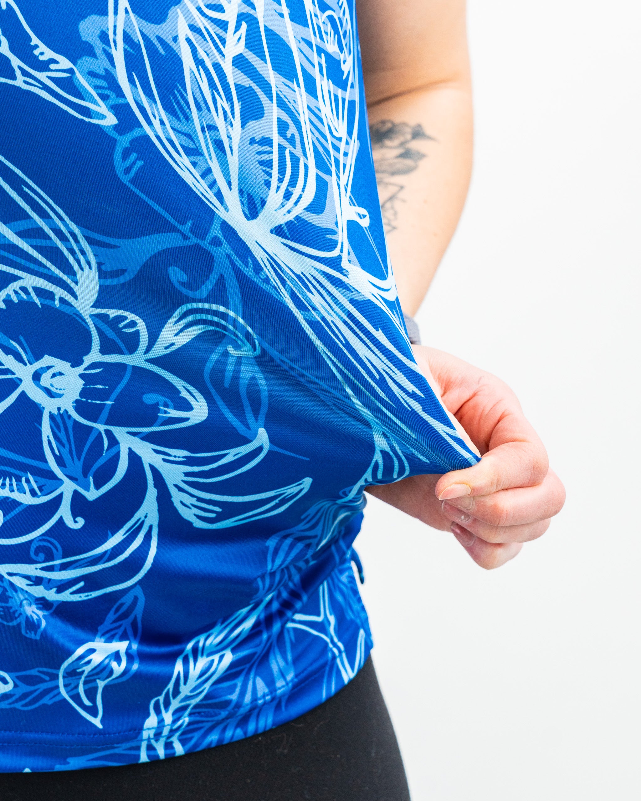 Close-up of a blue golf shirt with bold white floral and leaf patterns, worn by a golfer holding the hem.